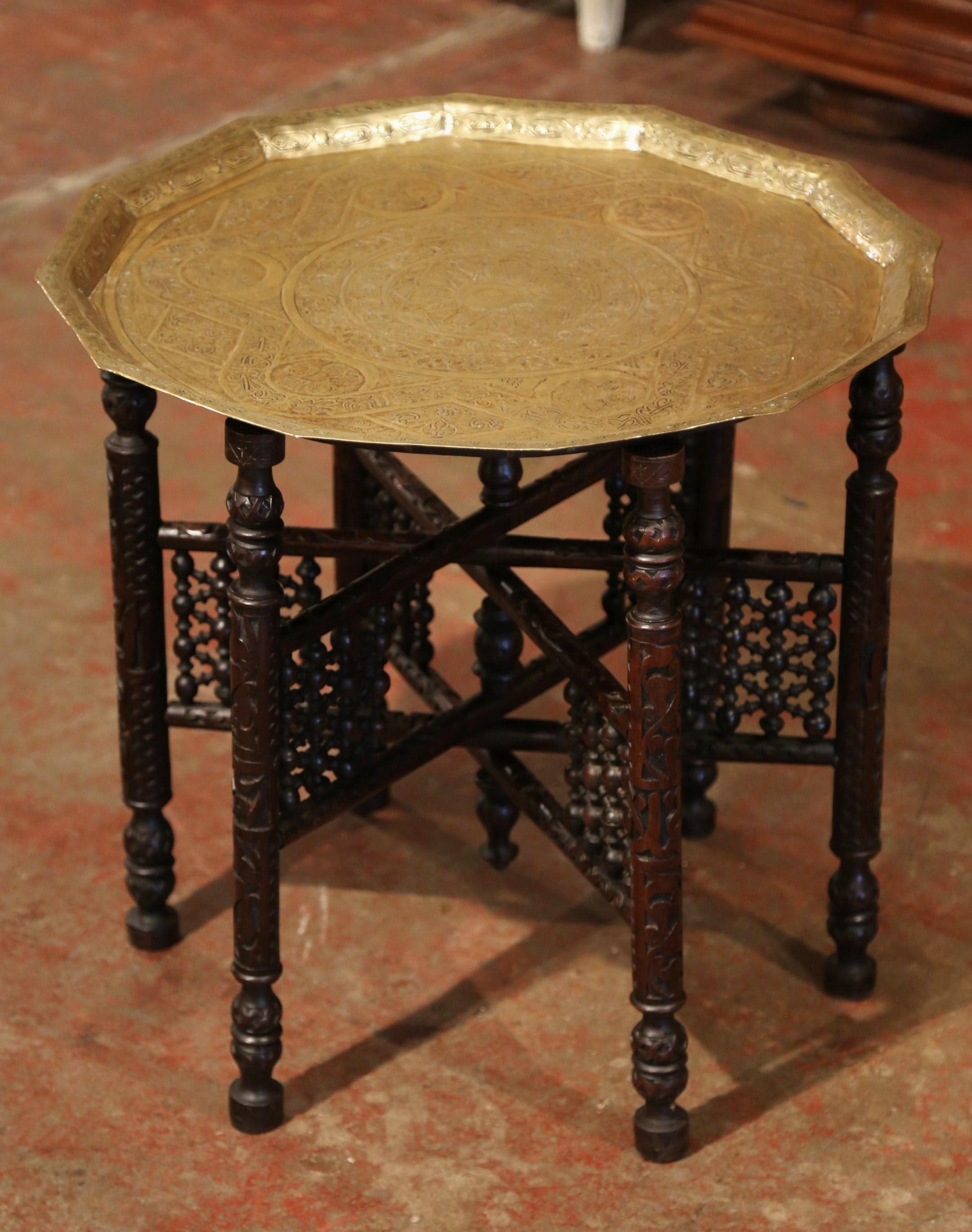 This small, versatile coffee table was crafted in Morocco, circa 1890. The folding base with decorative supports has six carved legs which can easily be folded up flat. The top features a twelve sided polygon brass tray top decorated with engraved