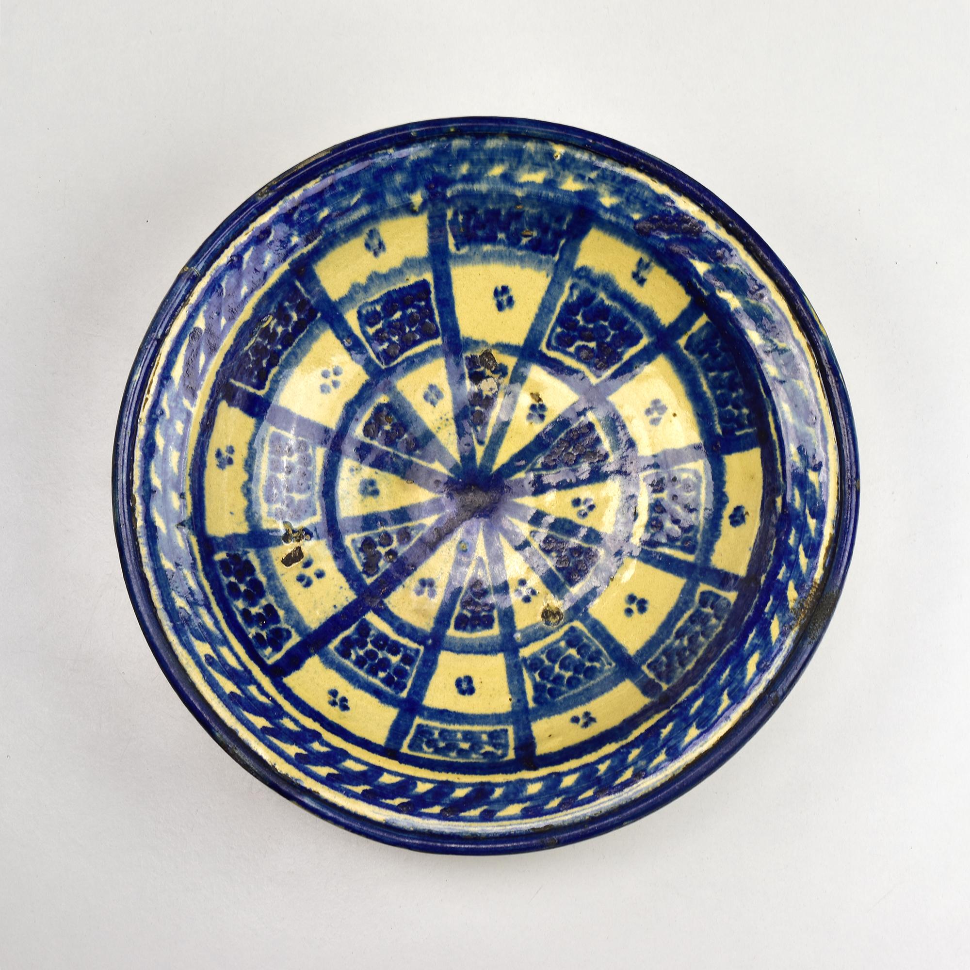 An antique 19th-century Moroccan ceramic bowl originates from Fez, a historic center of pottery craftsmanship. Handcrafted from terracotta and adorned with a striking cobalt blue and cream glaze, this footed bowl features an intricate radial
