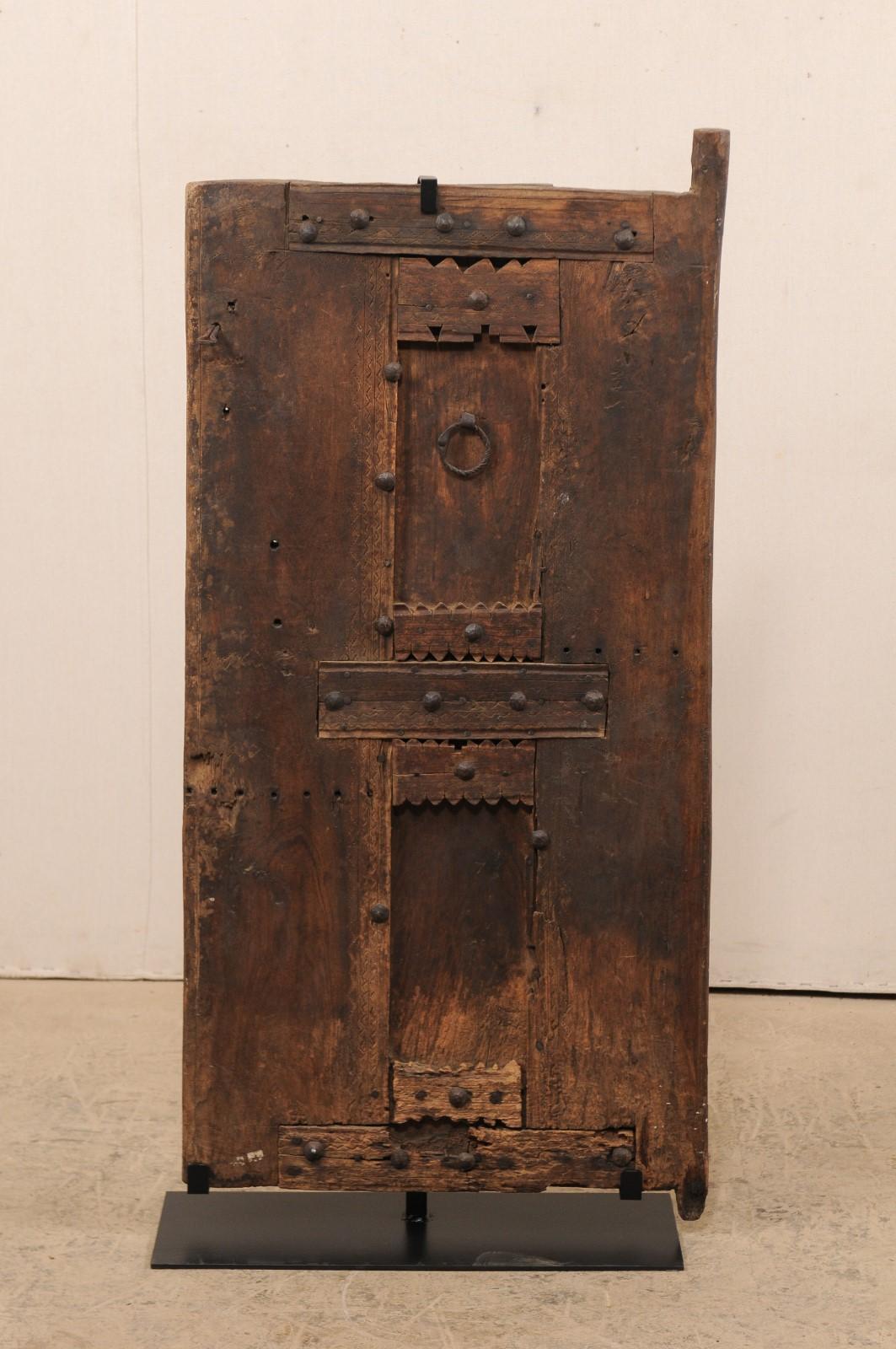 A Moroccan smaller-sized carved wood door from the late 19th century on custom stand. This antique door from Morocco has a wonderfully rustic appearance, with hand-carved accents and cut-outs adorning it's front side, and maintains its original iron