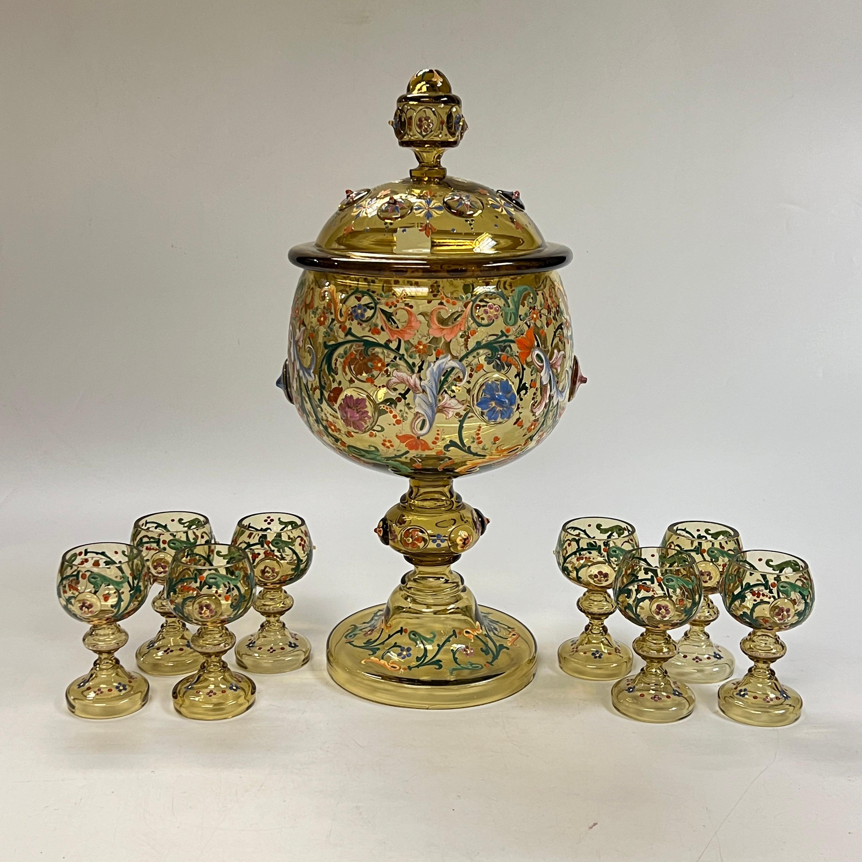 Très grand bol à punch en verre ambré avec huit (8) gobelets assortis, attribués à Moser, présentant des motifs en émail en relief comprenant des étoiles, des feuillages et des fleurs, et le couvercle portant l'inscription en émail blanc, Good Luck