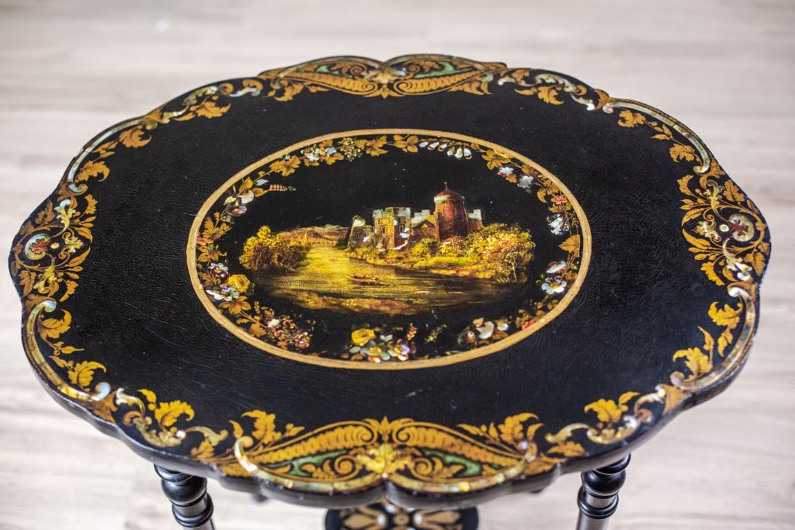 We present you a neat polychromatic end table with gildings and inlaid work.
The whole was manufactured in the first half of the 19th century.
The rounded legs are connected with an X-shaped stretcher.
The oval table top with wavy edges is