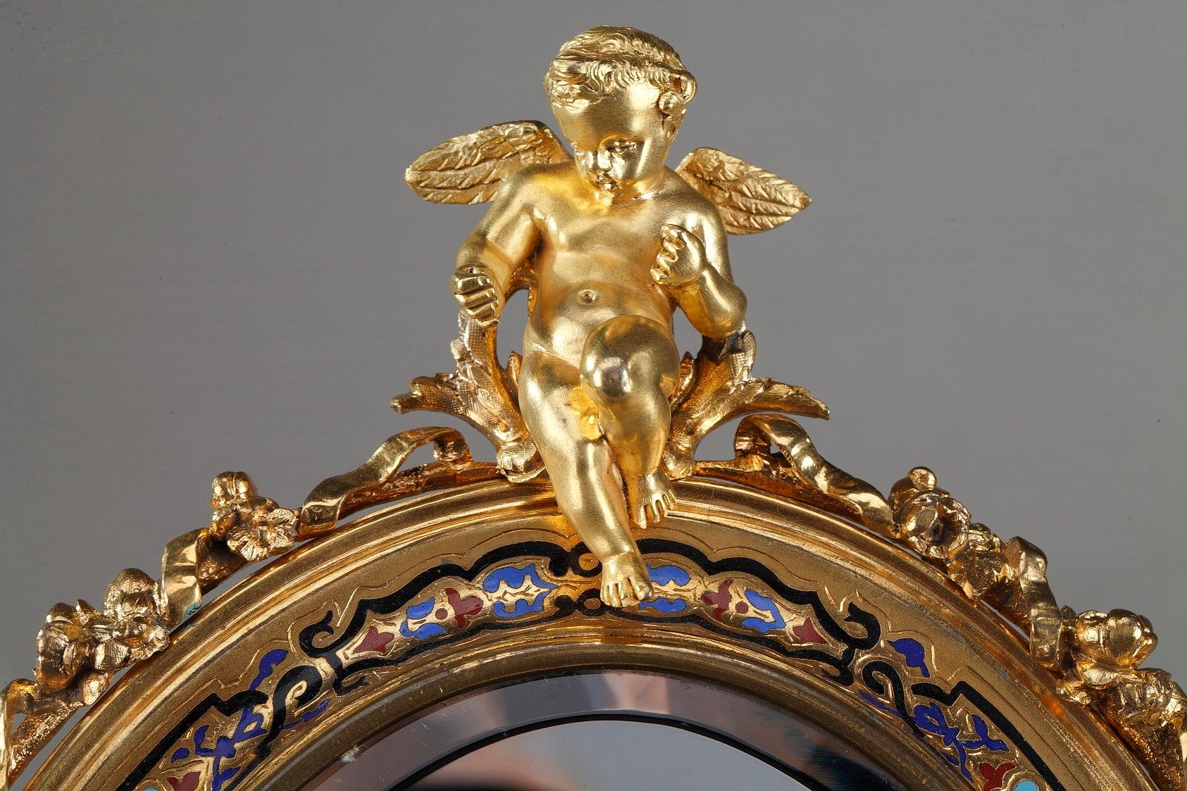 Small standing mirror with ormolu, or gilt bronze, frame covered in an exquisite design of champlevé enameling, with delicate interlacing and floral motifs. A gilt bronze winged putto adorn the top of this antique mirror glass. It is set on an