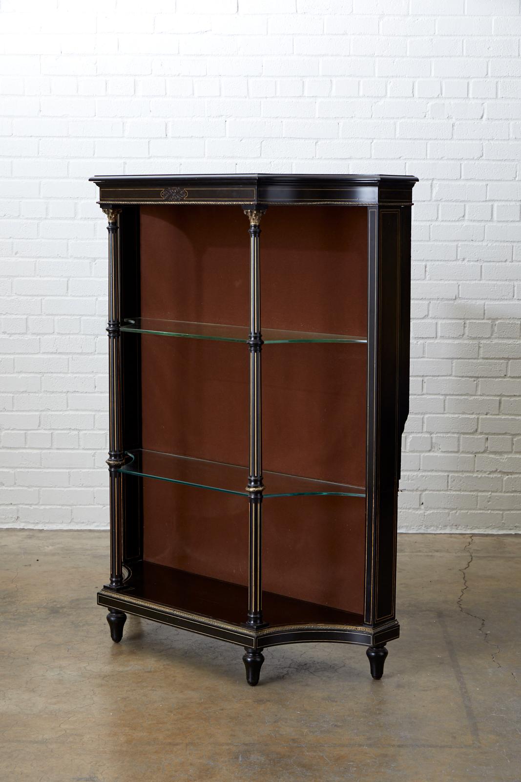 Dramatic 19th century French bookshelf or étagère featuring an ebonized case decorated with gilt string inlay. The piece has three glass shelves supported by bronze mounted neoclassical columns. Constructed in the French Napoleon III or Second