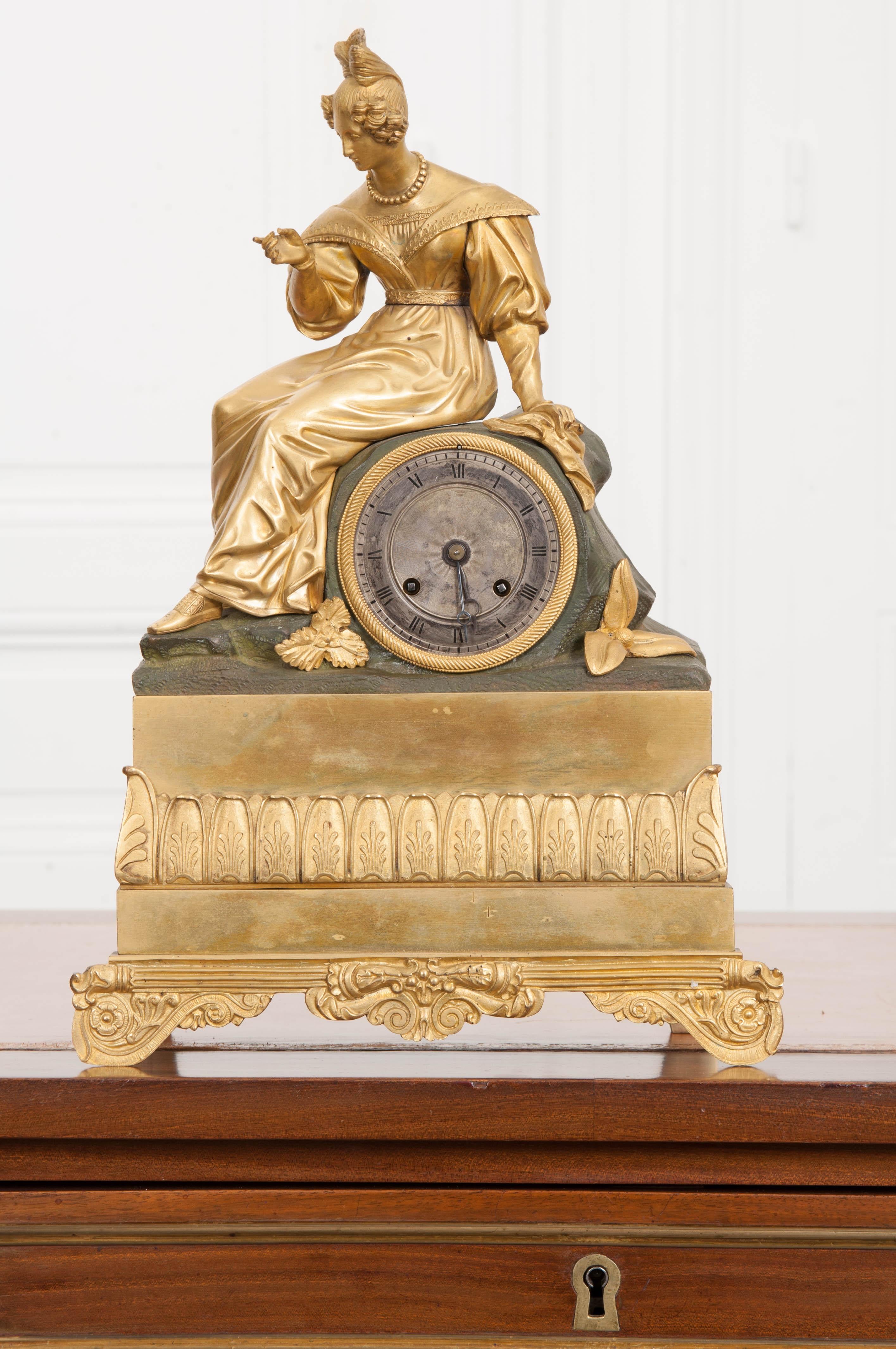 Diese wunderschön detaillierte Napoleon III feuervergoldete Bronze figurale Kaminsimsuhr ist aus Frankreich, ca. 1860-1880. Das Bild zeigt eine anmutige Jungfrau in klassischer Kleidung, die auf einem Felsen sitzt. Der Sockel ist mit einer