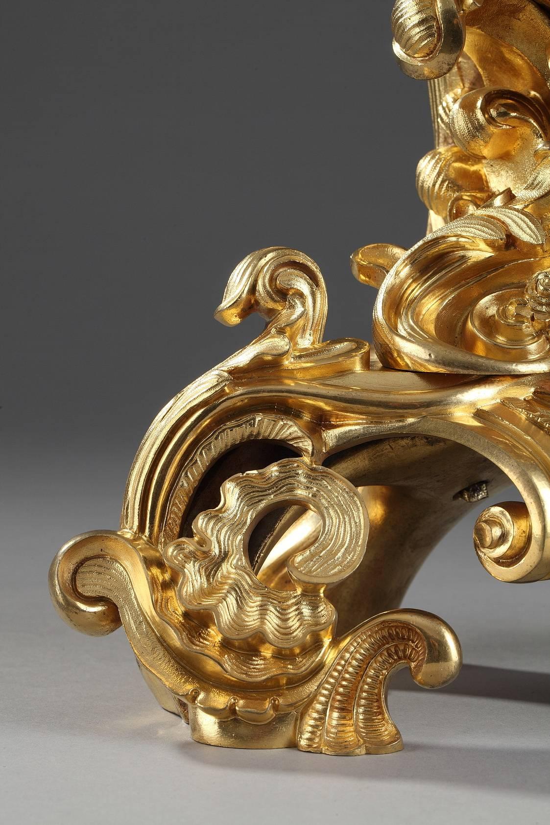 Petite pendule en bronze doré de style Rocaille, richement décorée de feuillages, coquillages et rinceaux. Le cadran émaillé blanc, avec des chiffres romains pour les heures et arabes pour les minutes, est surmonté d'un Cupidon assis sur une