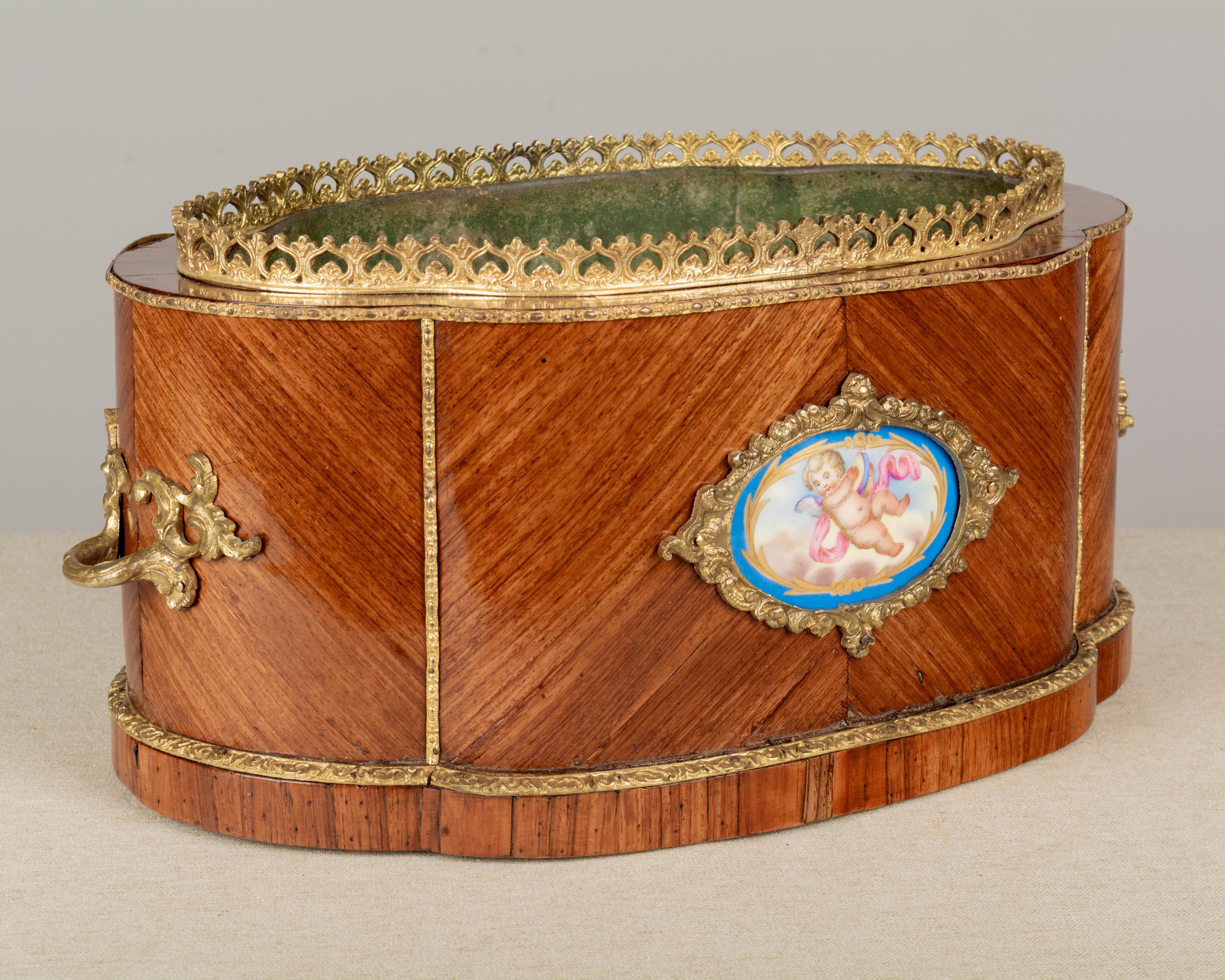 A 19th century Napoleon III bronze mounted marquetry jardiniere, or planter, with inlaid veneer of kingwood. Decorated with two hand-painted Se`vres porcelain medallions, one with a cupid and the other with flowers. Original removable zinc liner has