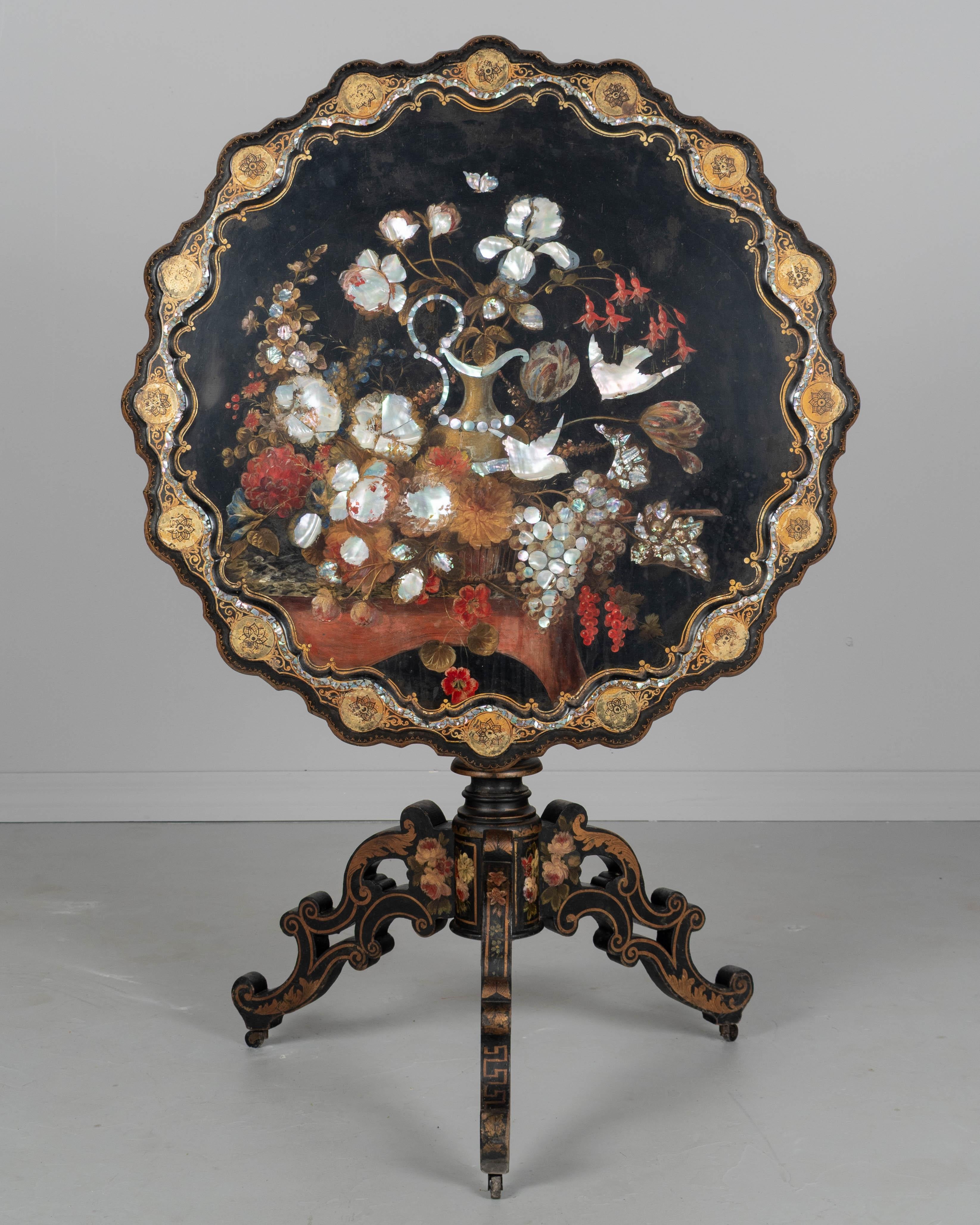 Un exquis guéridon français du 19e siècle de style Napoléon III. Ce guéridon présente un plateau laqué noir à bord festonné avec un décor floral peint à la main, des motifs rocaille dorés et des incrustations de nacre. La table repose sur une base