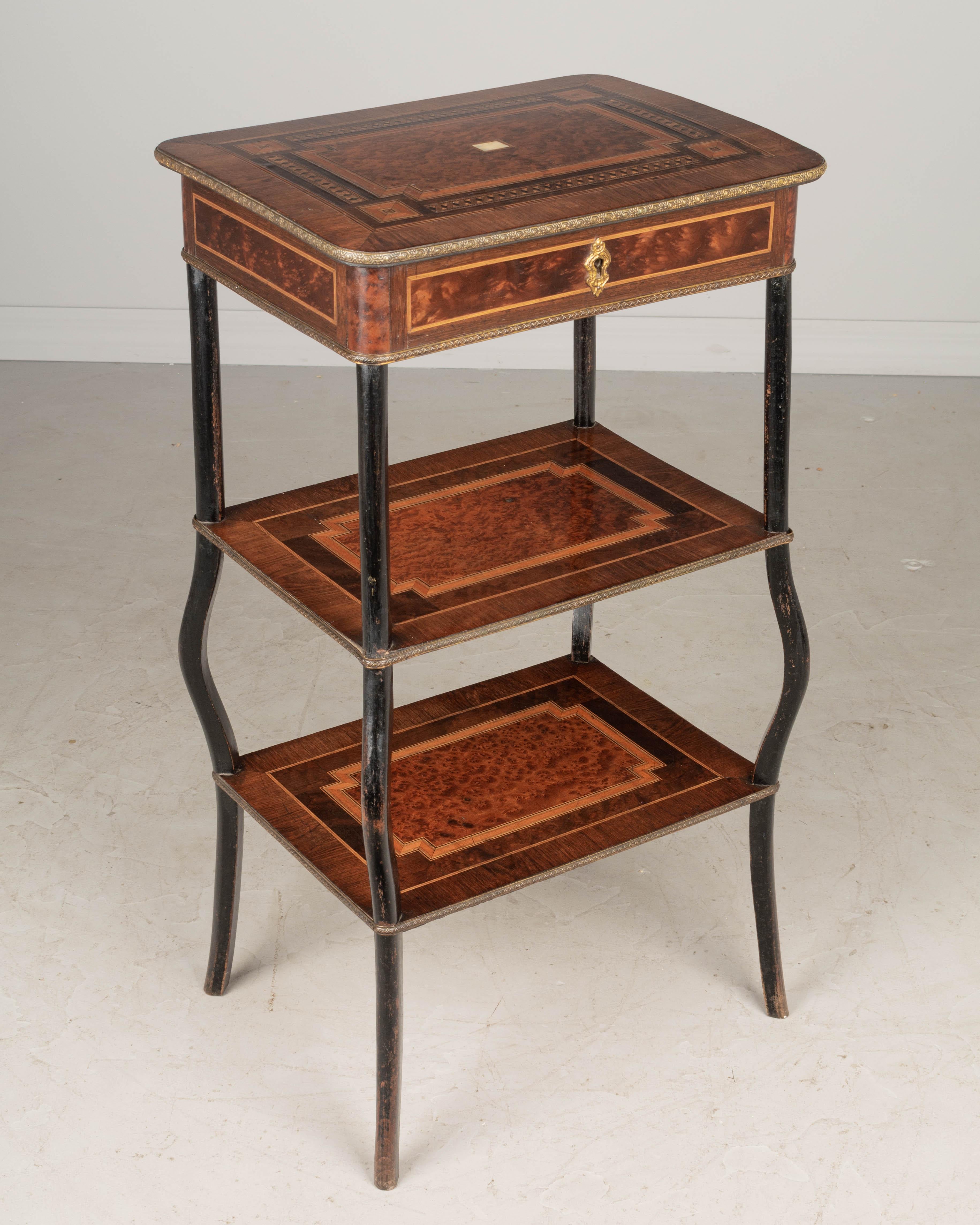 A late 19th Century French Napoleon III marquetry tiered table, hand-crafted with inlaid veneers of mahogany, walnut and burled walnut with inset mother-of-pearl and decorative brass trim. Finished on all four side with sturdy mahogany legs