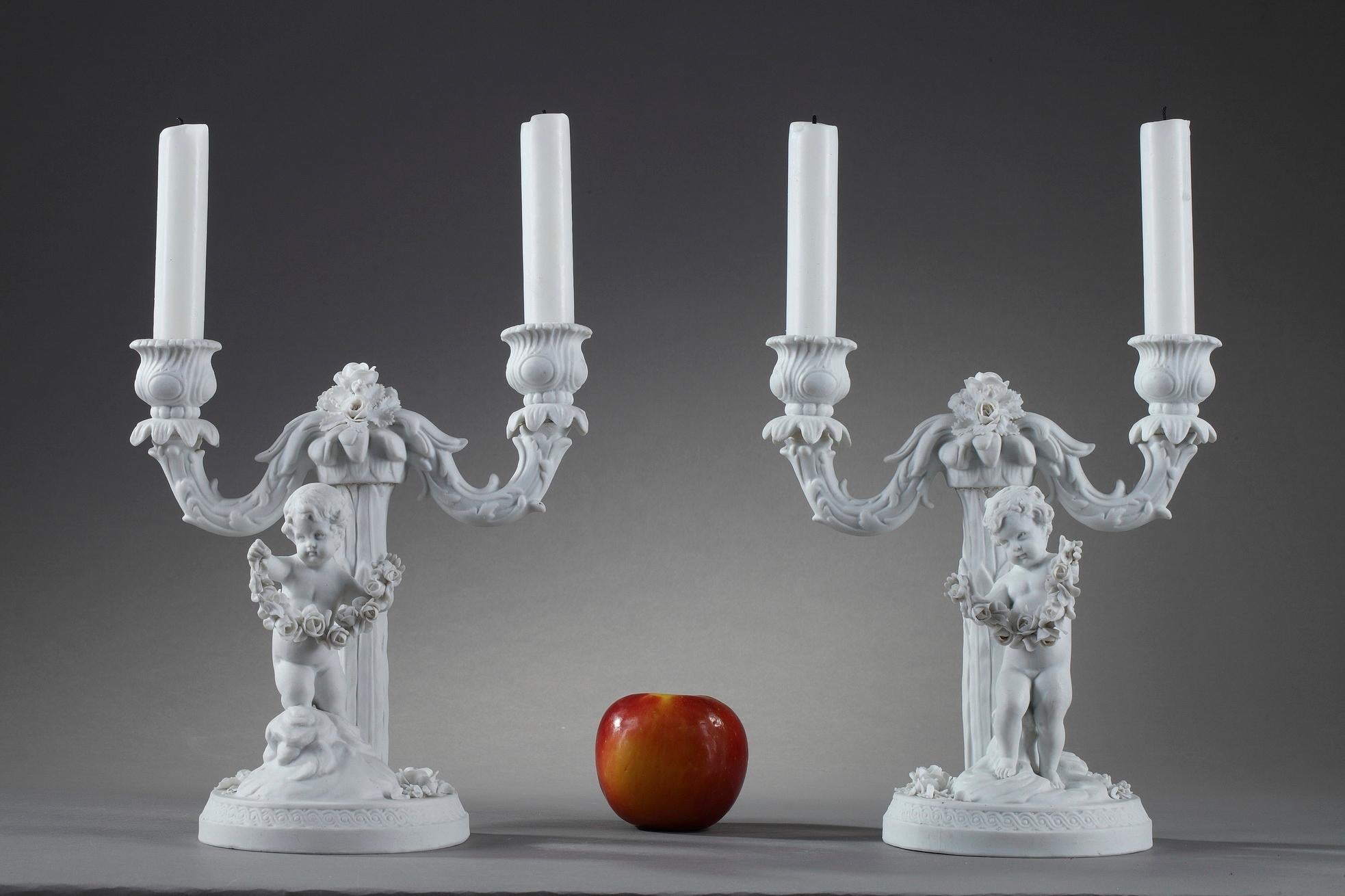 Pair of candlesticks in Sevres taste crafted of bisque porcelain with two lights. Influenced by the designs of Falconet at Sevres, each candelabra features a young Cupid on clouds, holding a garland of roses. Falconet Children were made at Sevres in