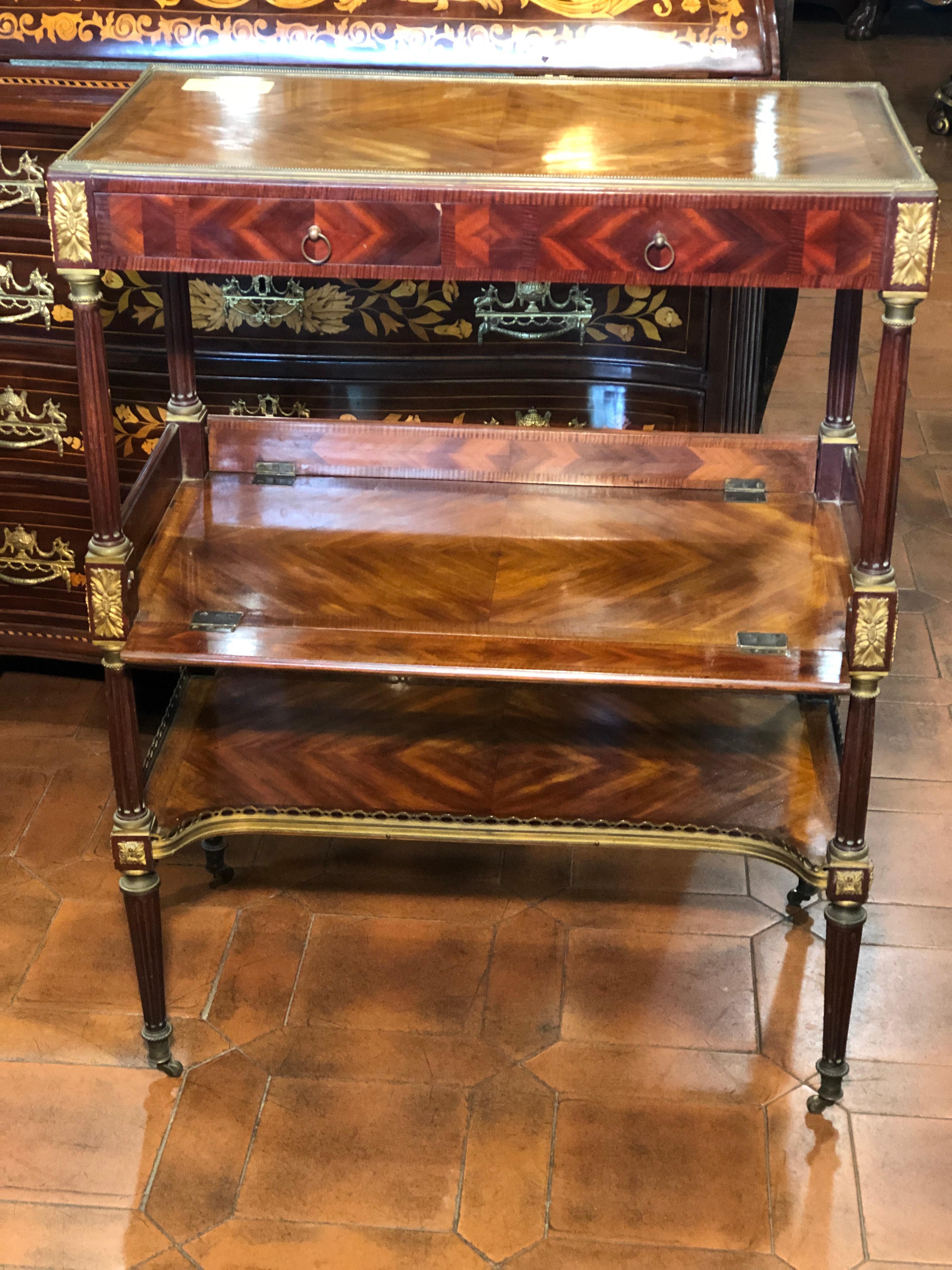 French étagère table, of incredible workmanship, hidden shelves, double lateral drawer alternating from a real and a fake one. Two underlying floors, one of which with folding edges, supported by double hinges. Contemporary bronzes and excellent