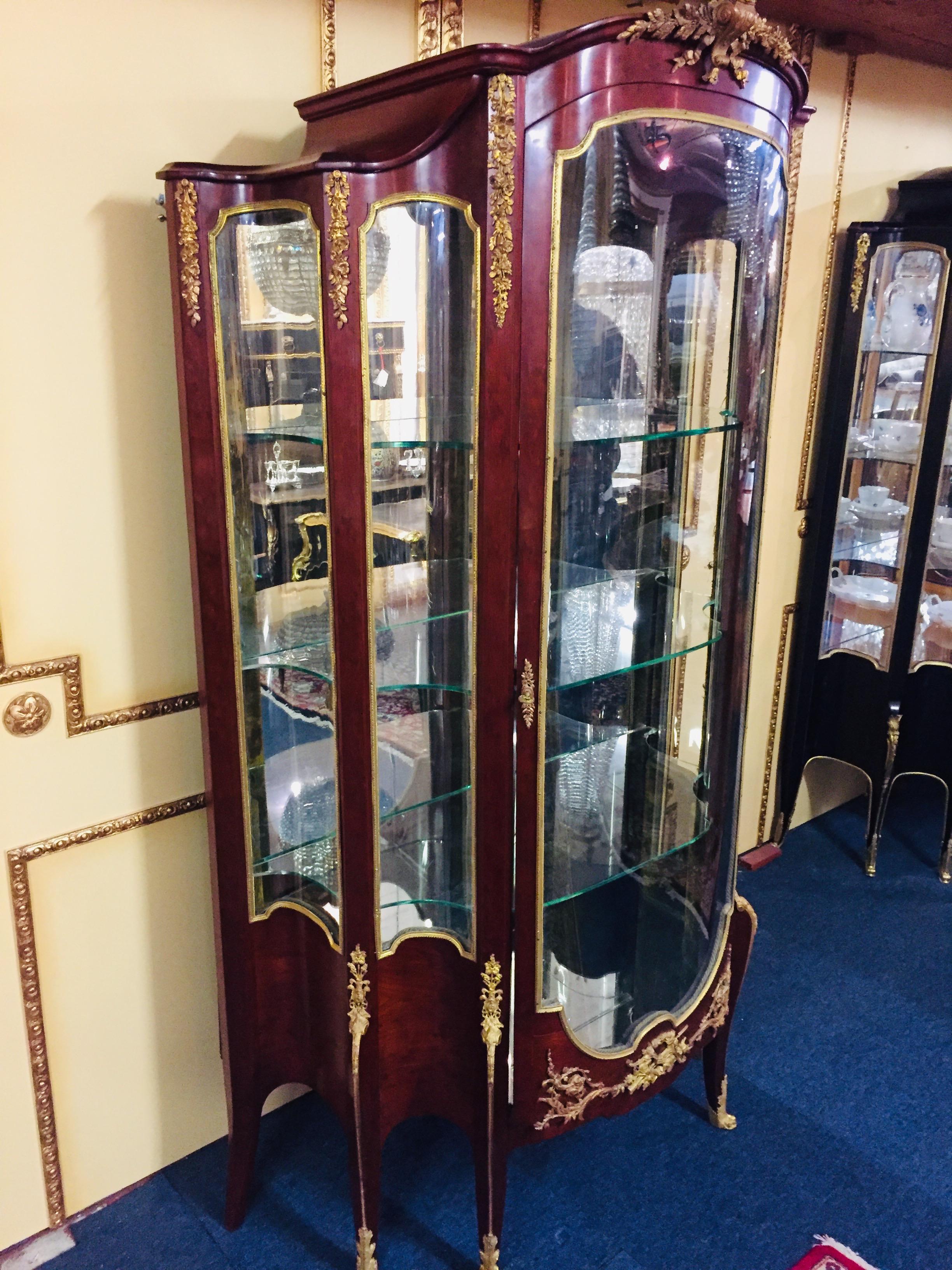 Majestic French vitrine Napoleon III in transition style, Paris. Rich in extremely finely chiselled, fire-gilt decorative bronze fittings. Mahogany on solid softwood. High-angled, one-door, cambered and three-sided glazed body on tall, slanting,