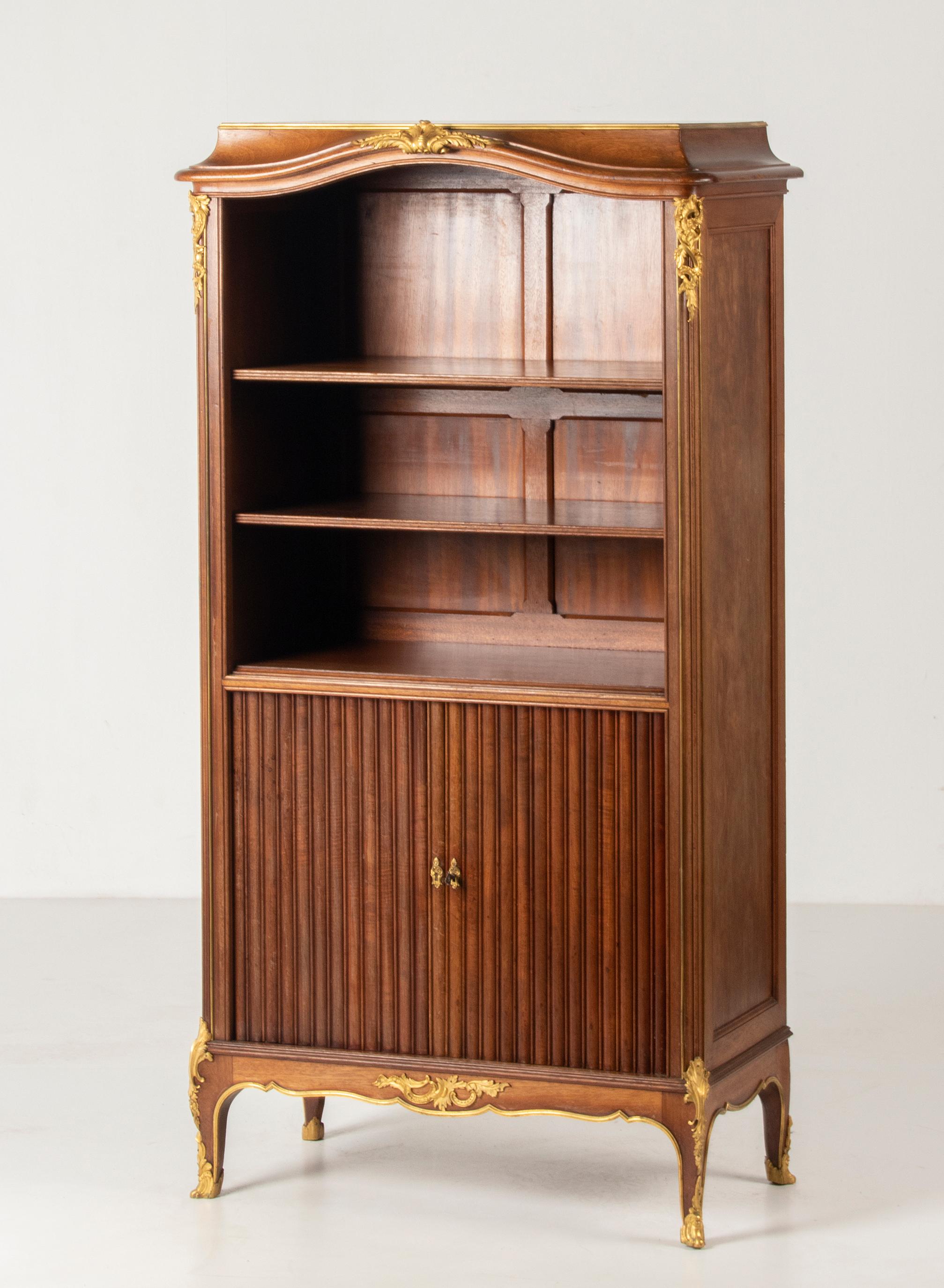 An antique French tambour door bookcase, made of solid mahogany wood. It's made in France, at the the end of the Napoleon III period, 1860-1870. The lower part has tambour sliding doors. The cabinet is embelished with ormolu gilt bronze ornaments.