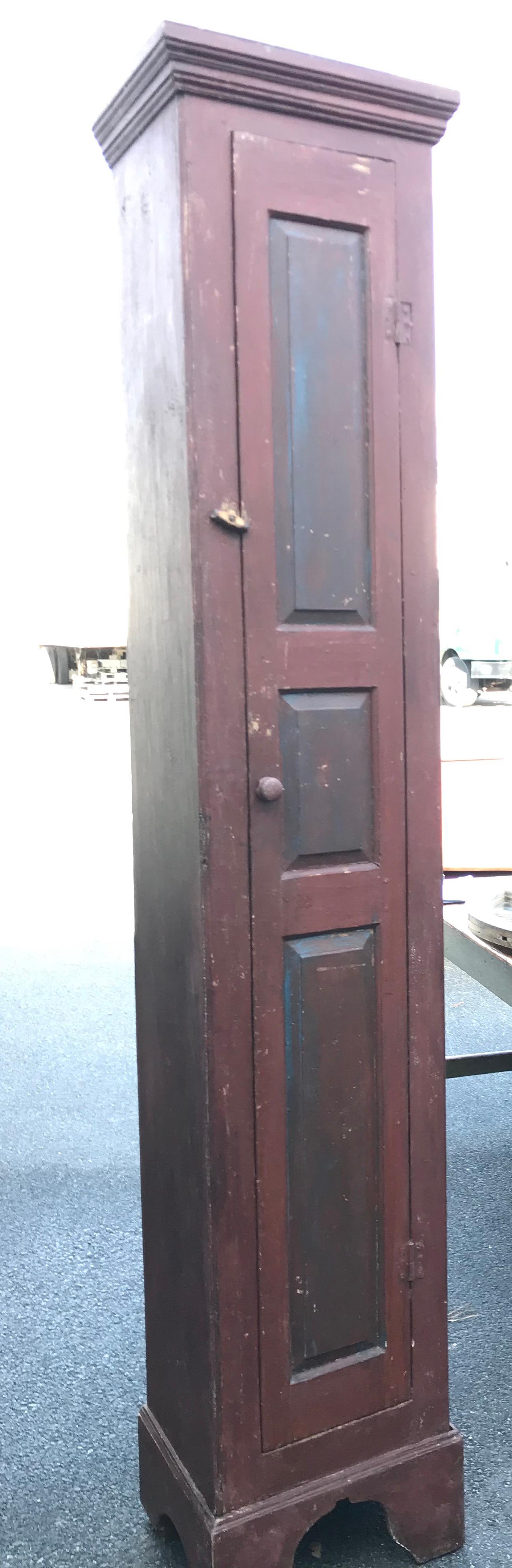 Mid to late 19th century Canadian Narrow Pine Chimney cupboard with stepped top over case with single door comprised of three vertically oriented raised panels, ending on bracket feet. Exterior in old red paint throughout with old red over blue