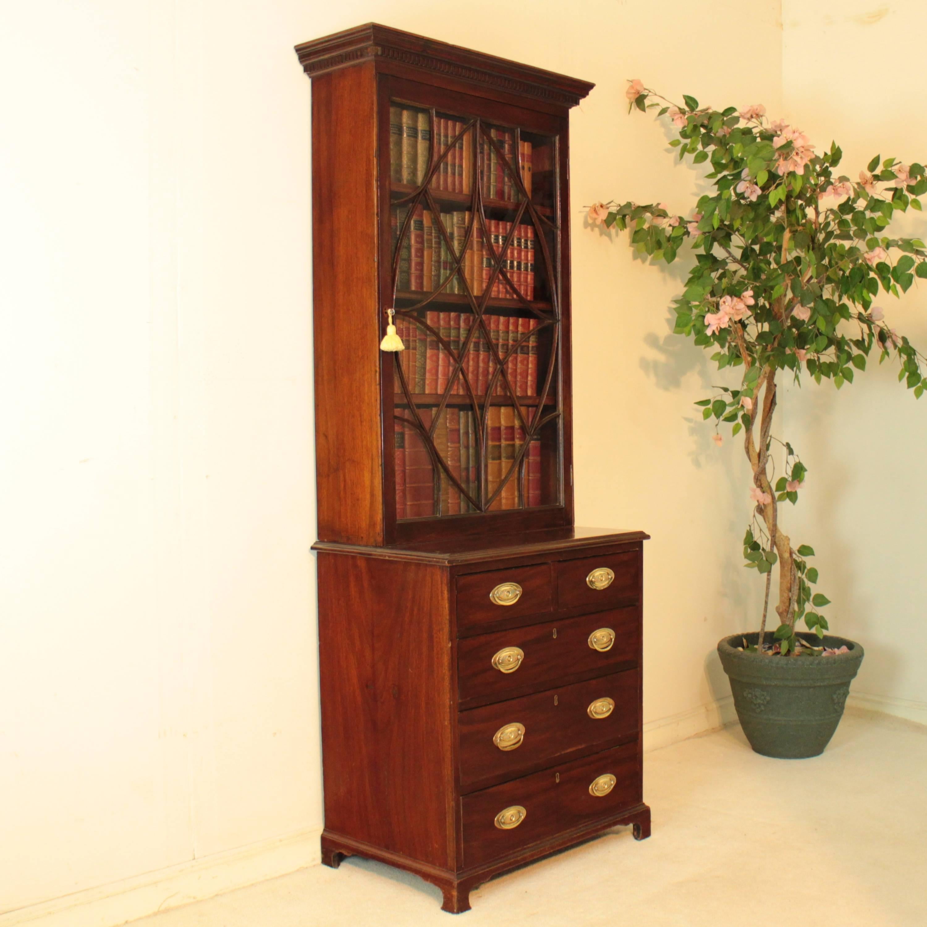 An unusual 19th century mahogany single door bookcase-on-chest of small proportions. With a moulded dentil cornice above a Hepplewhite style astragal glazed door enclosing three adjustable shelves, the projecting base has two short over three longer
