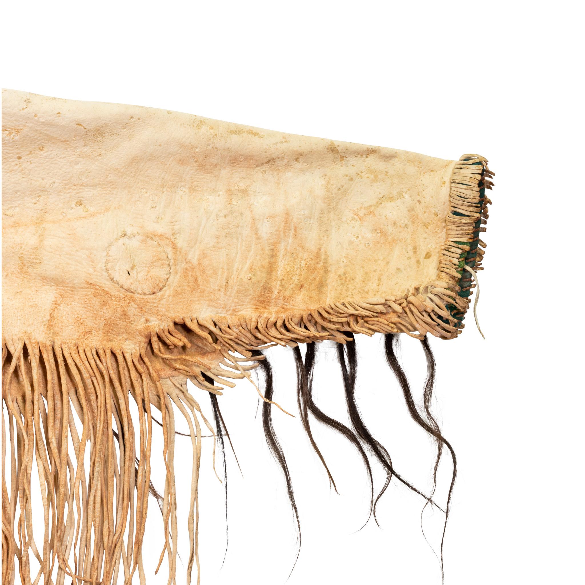 Chemise de guerre sioux du 19e siècle représentant un bison tanné à la cervelle et des mèches de cheveux enveloppées de plumes d'ocre rouge. Les bandes de perles sont ornées de têtes de bison stylisées, de pipes et de tipis. Belle patine d'usage à