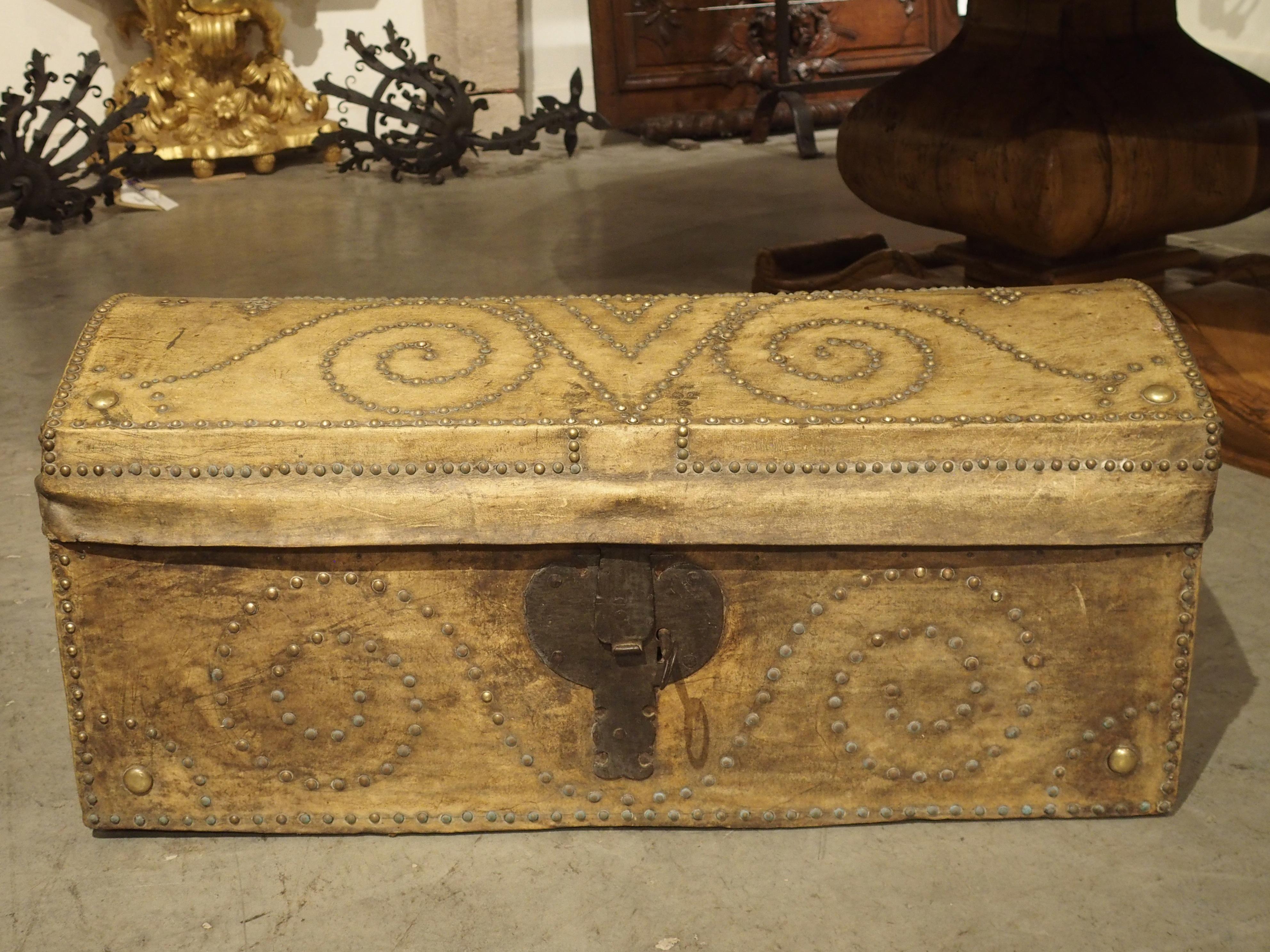 This unique leather and brass studded arcon, or Spanish trunk, is from the 1800’s and has been lined with a foliate fabric. The natural leather is a light golden color that meshes well with the brown, beige, and cream interior. Remnants of the