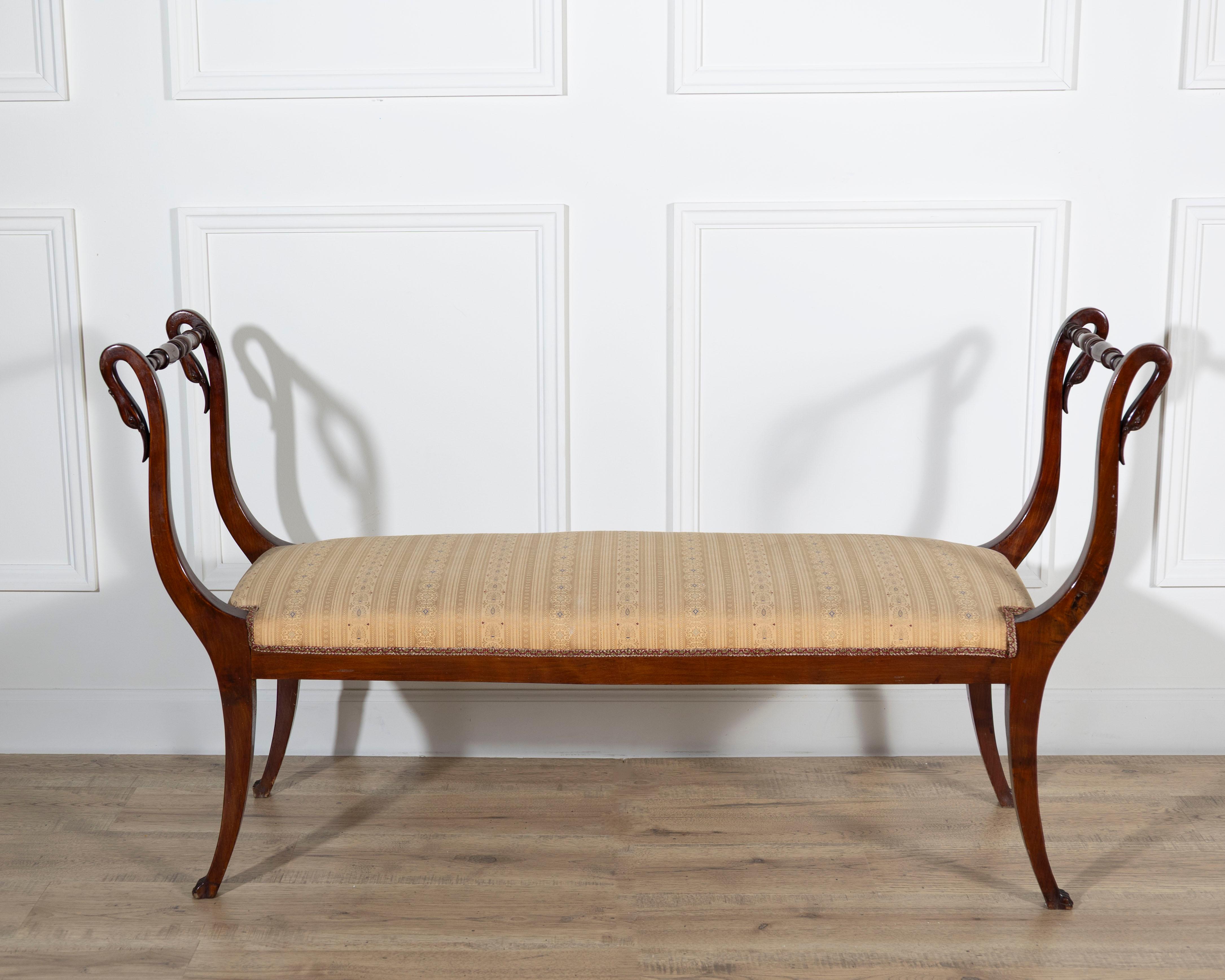 An elegant Neapolitan Empire bench crafted in solid mahogany, dating to the second half of the 19th century. Exemplifying the refined grandeur of southern Italian Empire design, the bench features gracefully curved armrests ending in finely carved