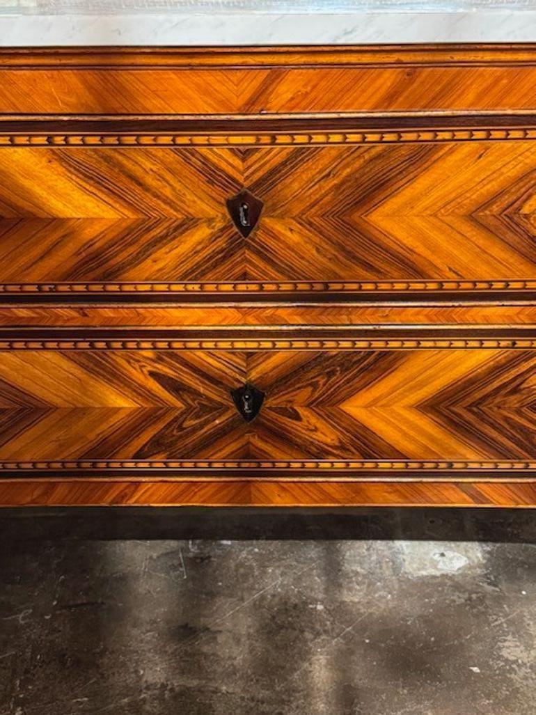 Questa commode neoclassica del XIX secolo presenta una splendida finitura in noce intarsiata con un lussuoso piano in marmo, che la rende un pezzo d'antiquariato davvero squisito. Il design classico è messo in risalto dall'intricato lavoro di