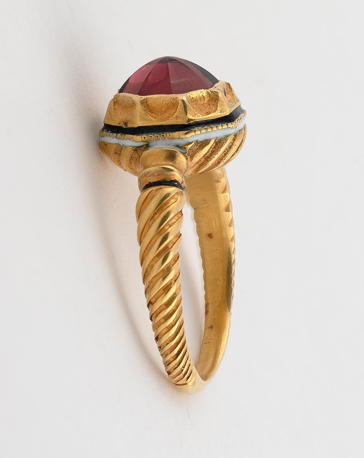 Cabochon red tourmaline in an elaborate high collet setting, between fluted shoulders, both with enamel decoration, ring size 7