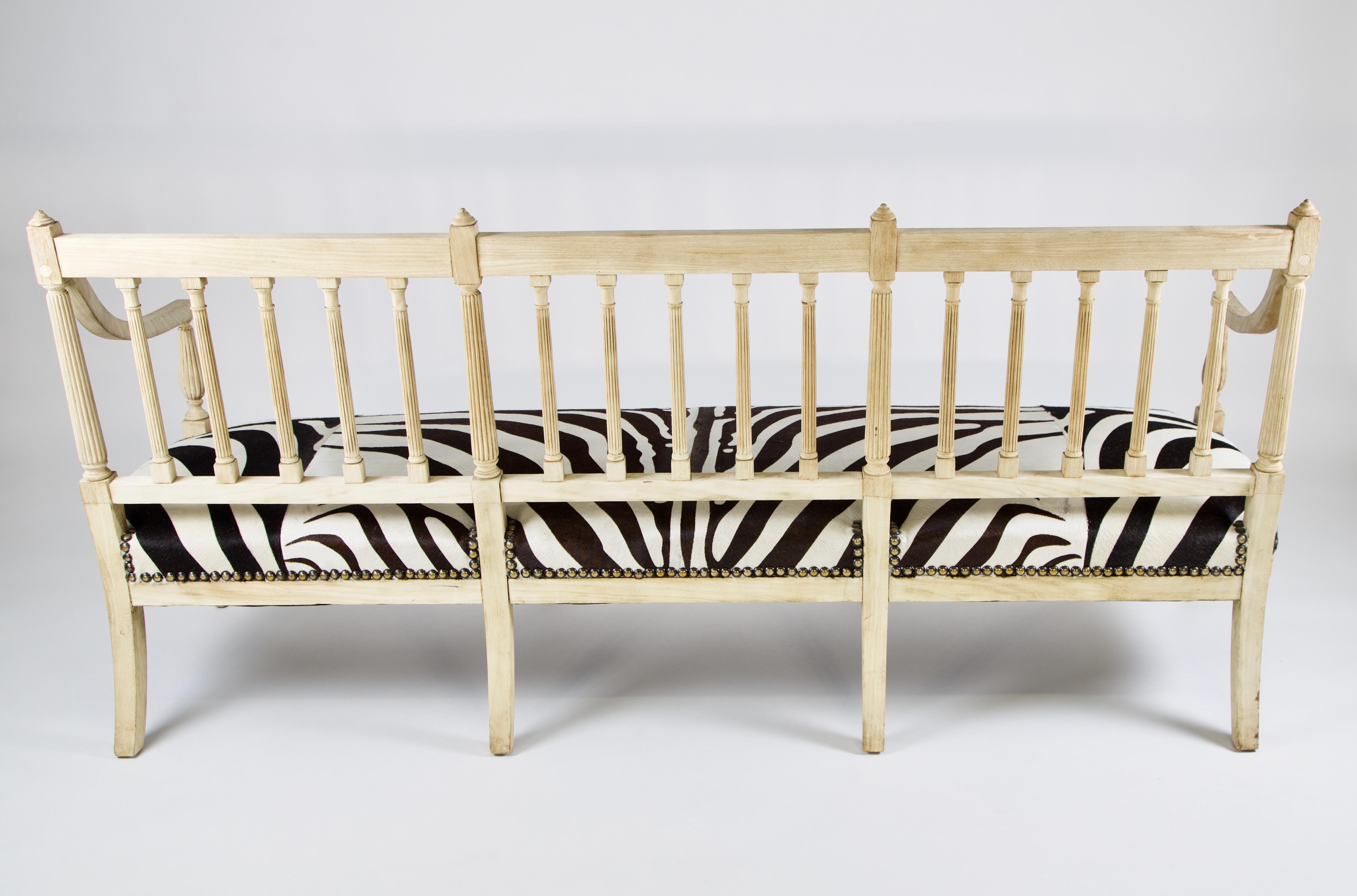 This is a 19th century neoclassic solid bleached  mahogany bench from the mid-1850s. It has spindle back with reeding on the legs with a gentle curve to the arms. It has a 8 way hand tied seat which has been reupholstered with a zebra cow hide and