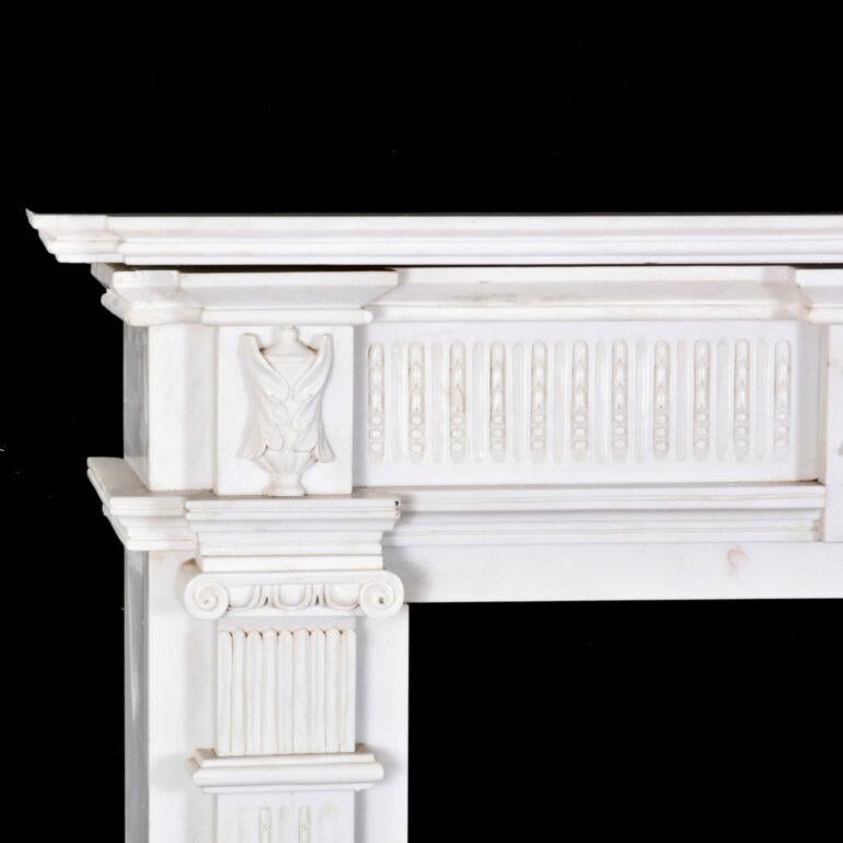 A 19th century neo-classical Carrara marble fire surround or mantlepiece, the sides in the form of fluted pilasters with ionic capitals and with a carved urn in the centre.

