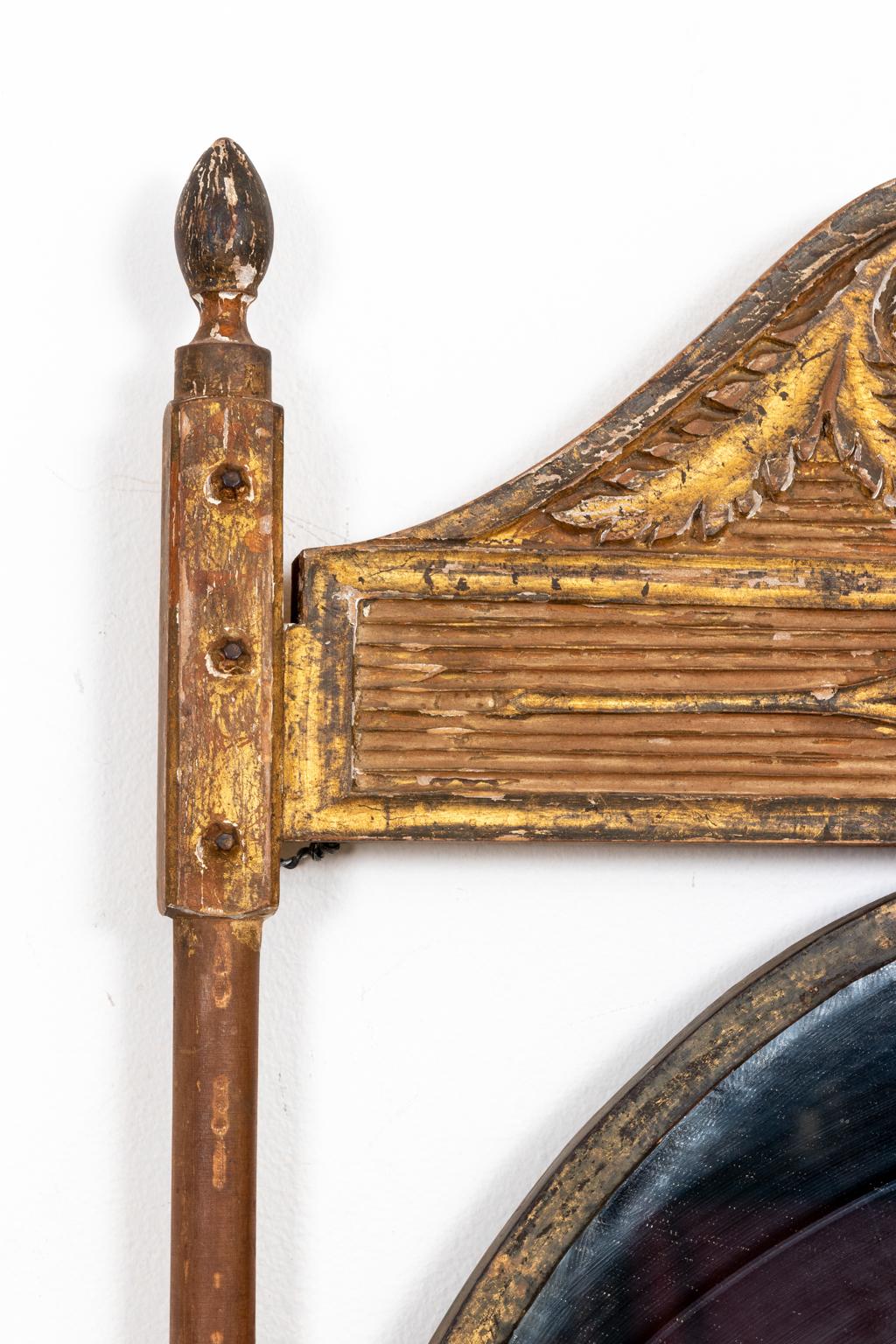 Circa 1820s Neoclassical style carved and gilded mirror with original patina on crisply carved wood with traces of gilded over bole and gesso. The piece was probably originally used as a sign as seen in the metal center oval, now replaced with a
