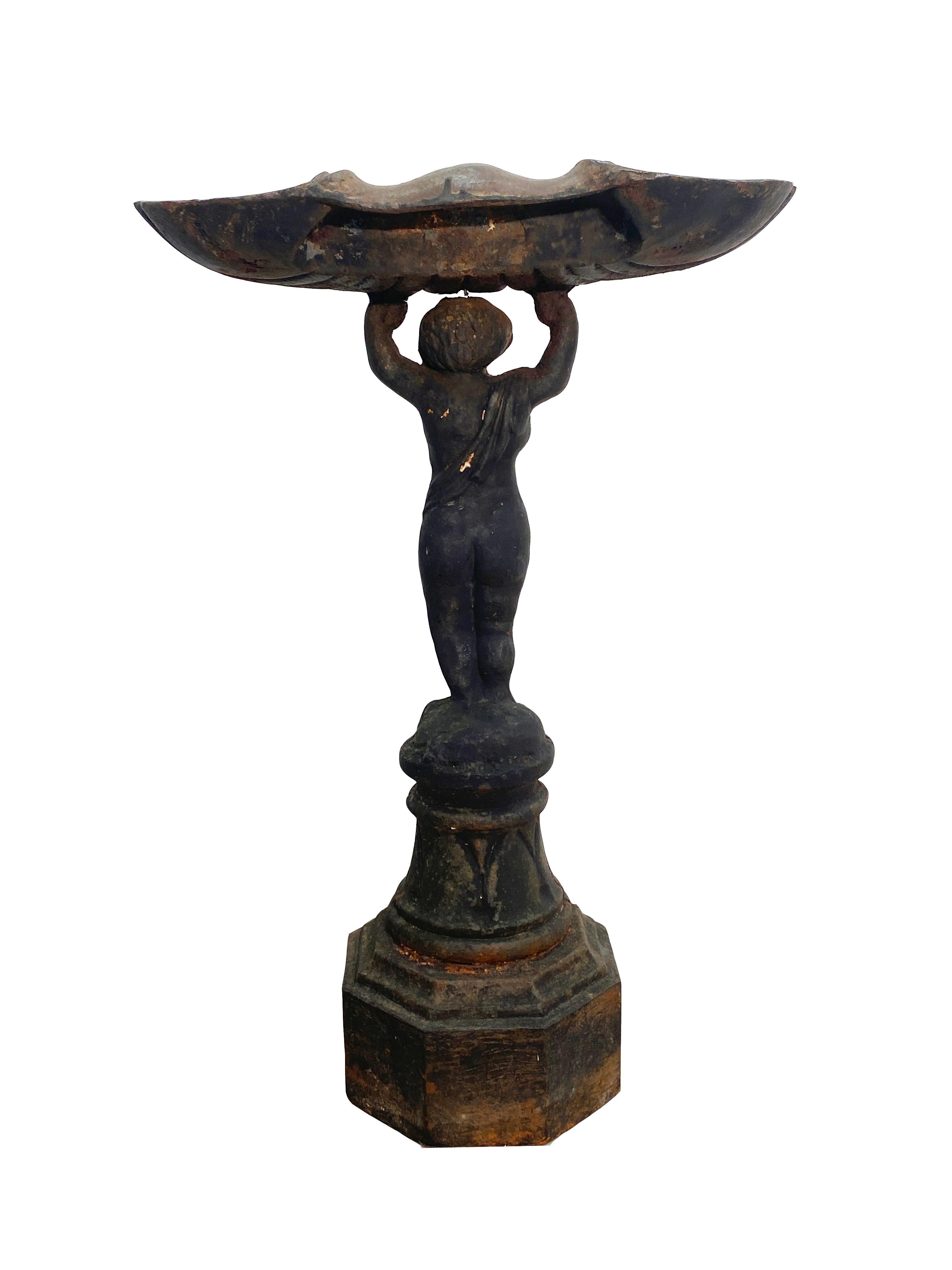 Late 19th century heavy patinated cast iron bird bath in New Classical style. Cherub standing atop an octagonal base raising a shell form basin.