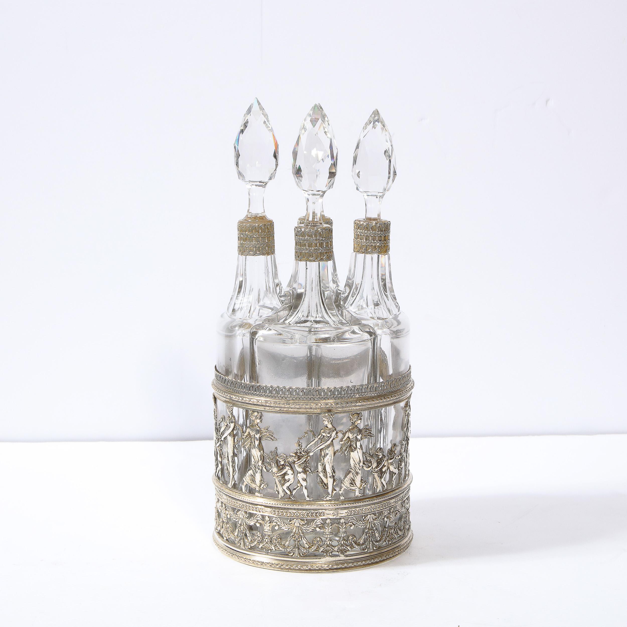 This elegant and regal fitted silver plate and cut crystal decanter set was realized in England during the 19th century. It features a cylindrical base replete with an abundance of neoclassical details in relief. The lowest band of the base offers