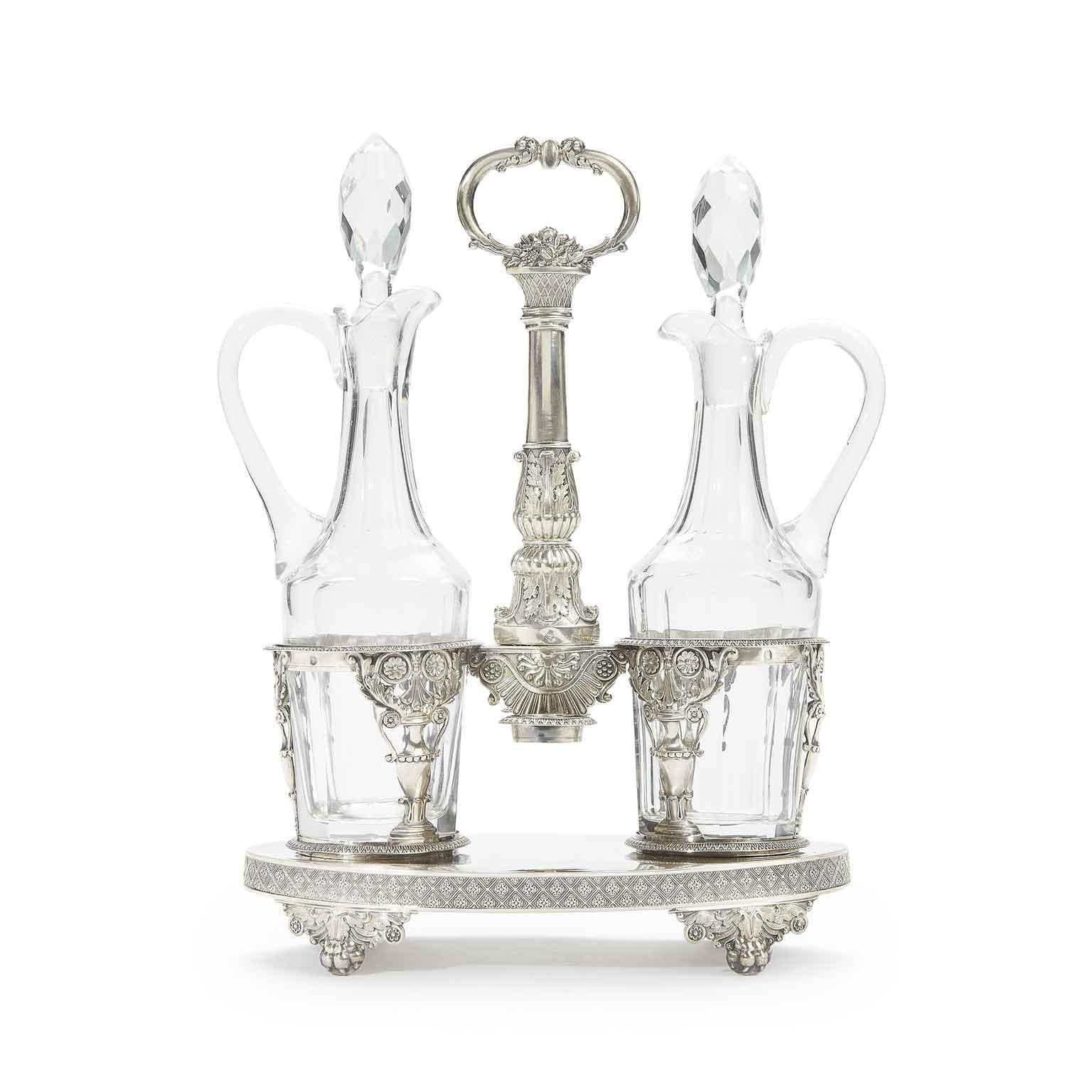 An antique sterling silver oil and vinegar cruet set, having a neoclassical style oval stand with hand-pierced and engraved flower and foliate decoration, with ring handle and a frame for two cut-glass cruet bottles probably later. Richly decorated