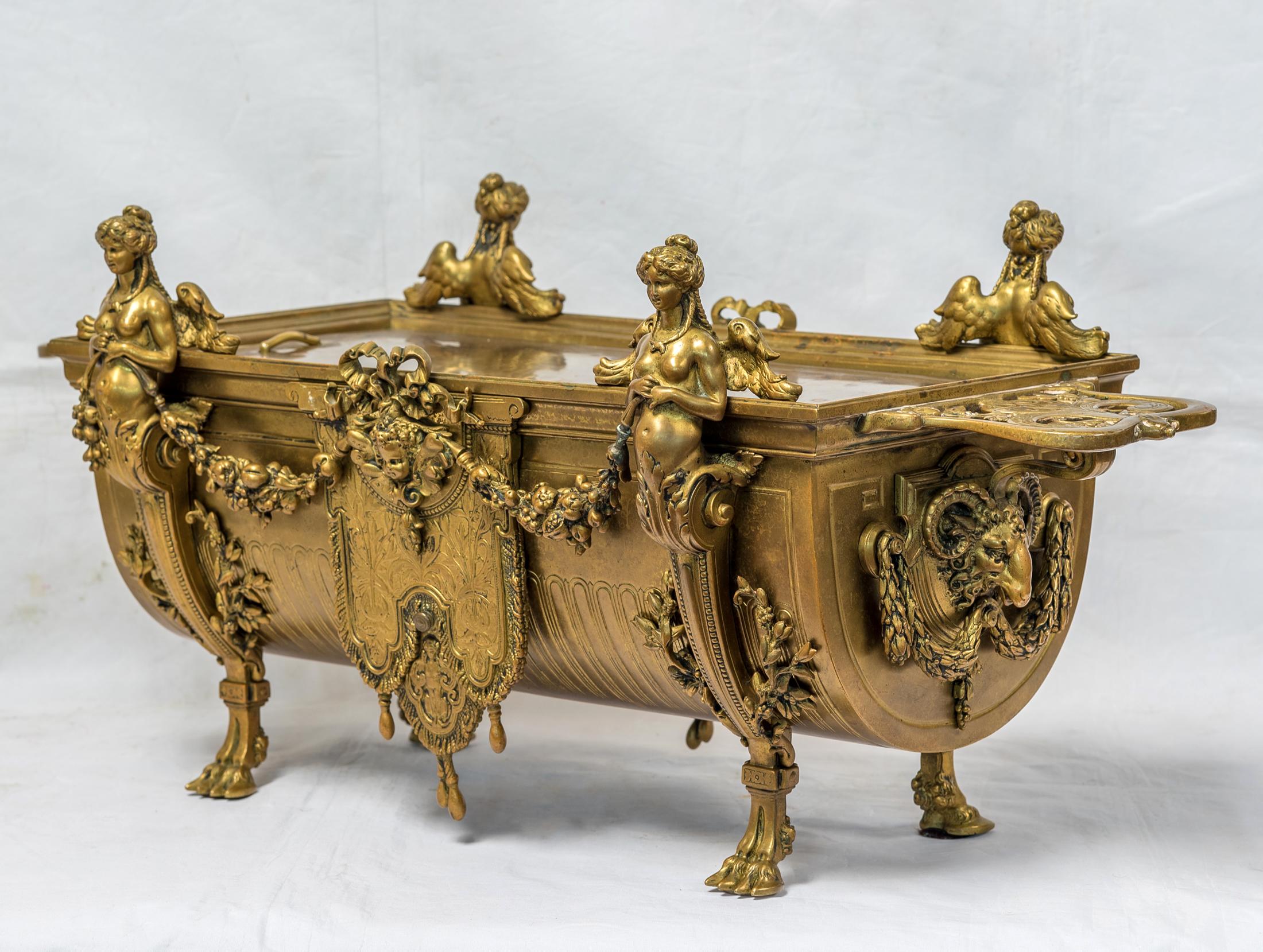 Un élégant centre de jardinière néoclassique français en bronze doré.
Les poignées ajourées et façonnées reposent sur des supports féminins ailés se terminant par des pieds en sabot flanquant des masques de putto suspendant des guirlandes, de forme