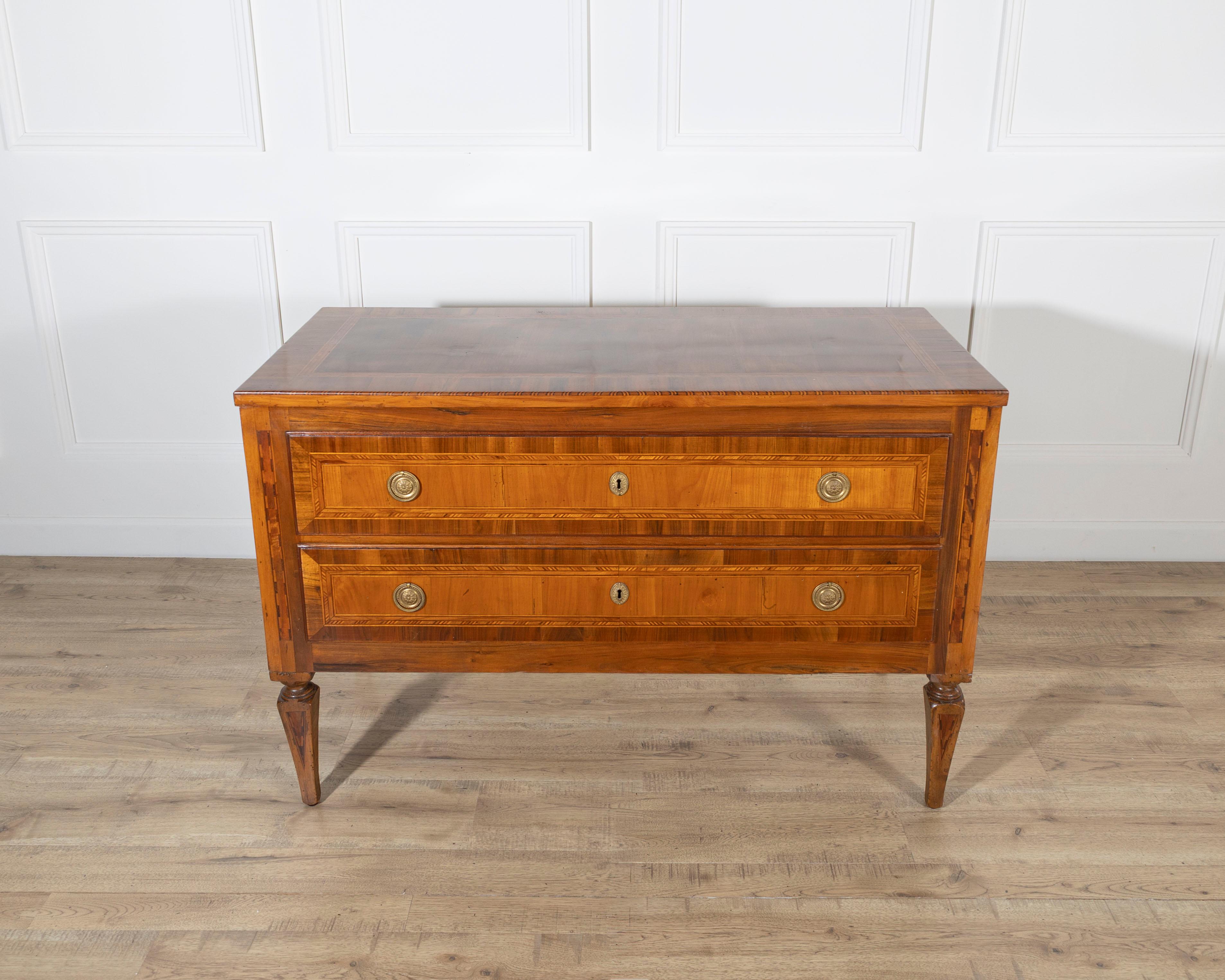 Una raffinata cassettiera neoclassica in noce e ciliegio, che si distingue per i ricchi intarsi e le proporzioni equilibrate. La facciata presenta due ampi cassetti, ciascuno dei quali è filettato e incorniciato da delicate fasce di acero, mogano,