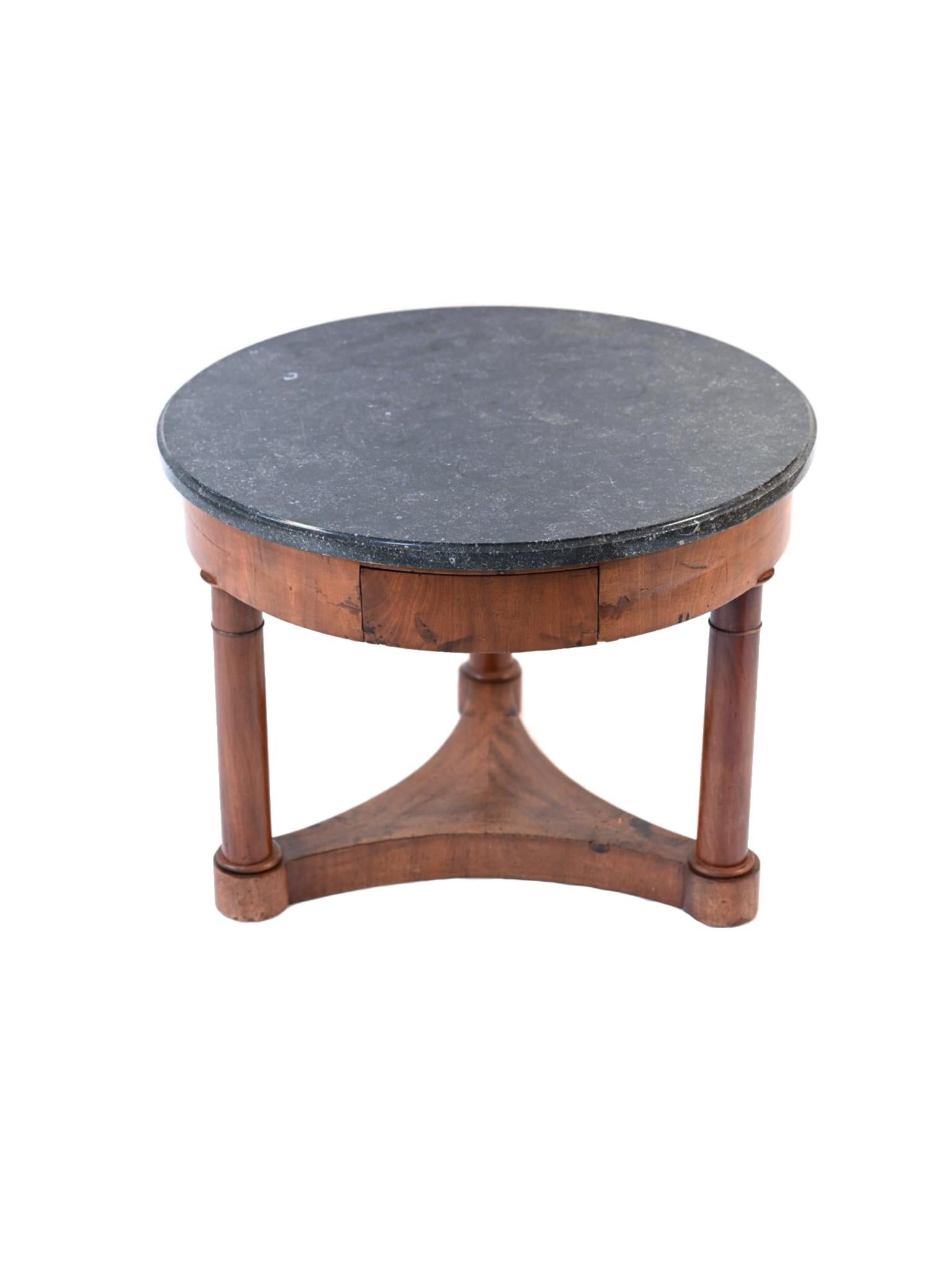 This 19th century French Empire round table is comprised of a mahogany base and a round marble top. There's a single, small drawer. The style is Neoclassical, harking back to the symmetry and balance found in ancient Greco-Roman design. It's a