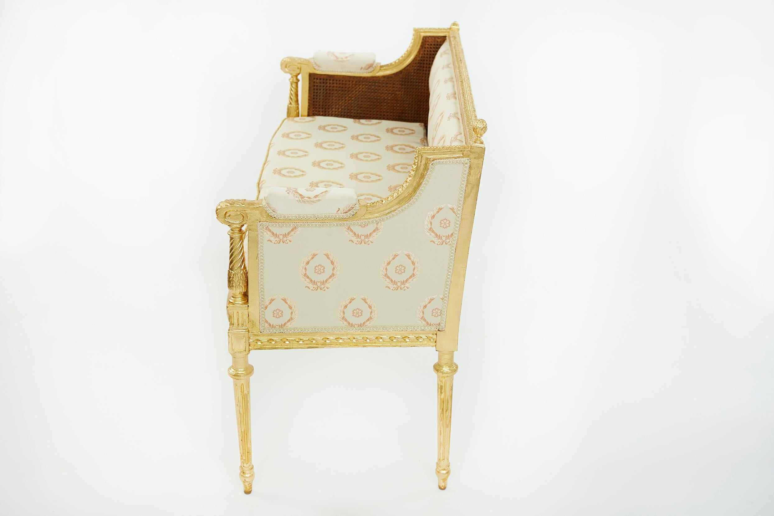 Beautiful Neoclassical style gilt wood framed hand carved settee with caning back panel. The seat is recovered with a cream damask upholstery with laurel wreath motif. The settee is in good condition with minor wear consistent with age / use. The