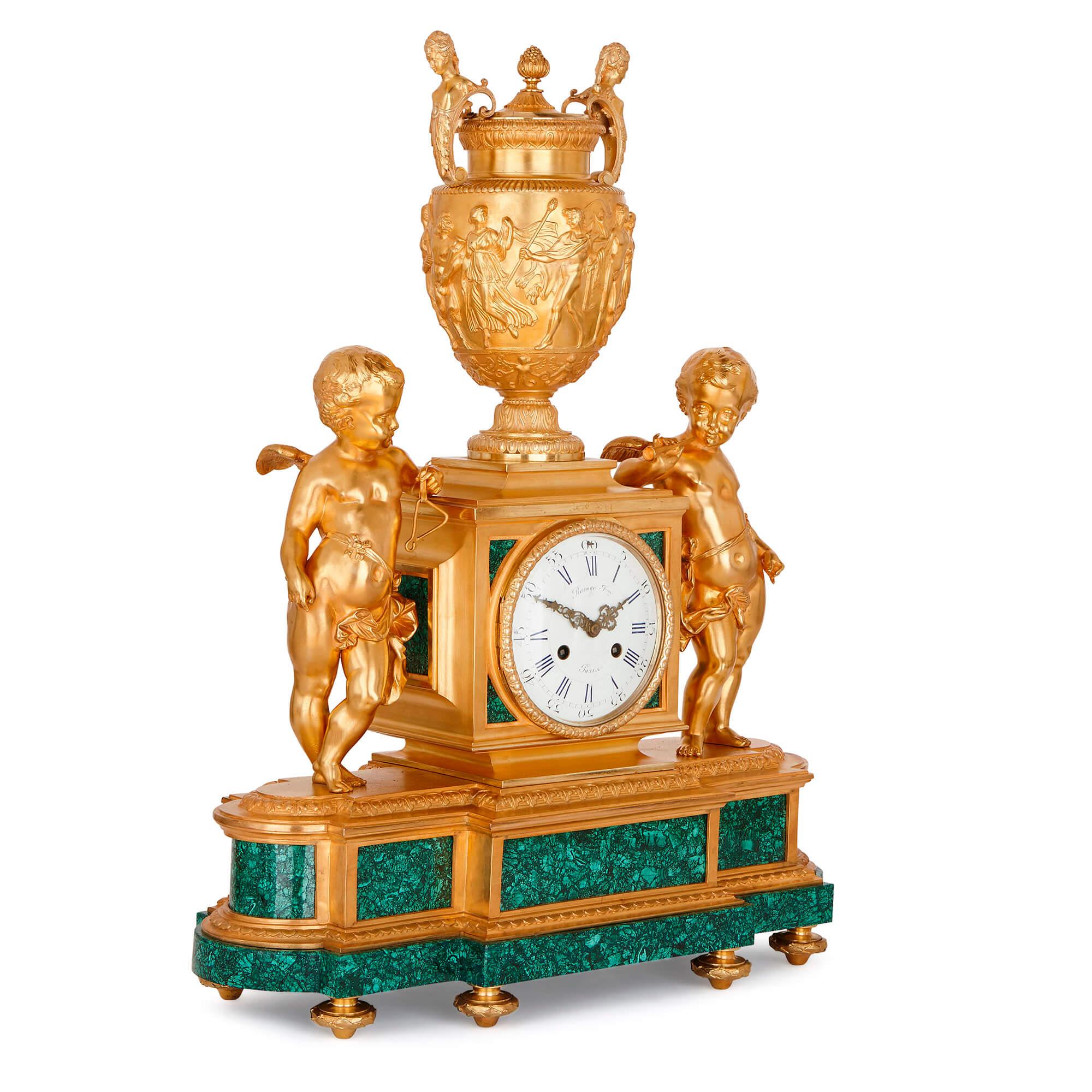 This charming neoclassical garniture is formed of a clock and two flanking vases on pedestals. The clock, positioned at the centre of the set, is fitted with an enamel dial and set on a malachite base. Flanking the clock face on either side are two