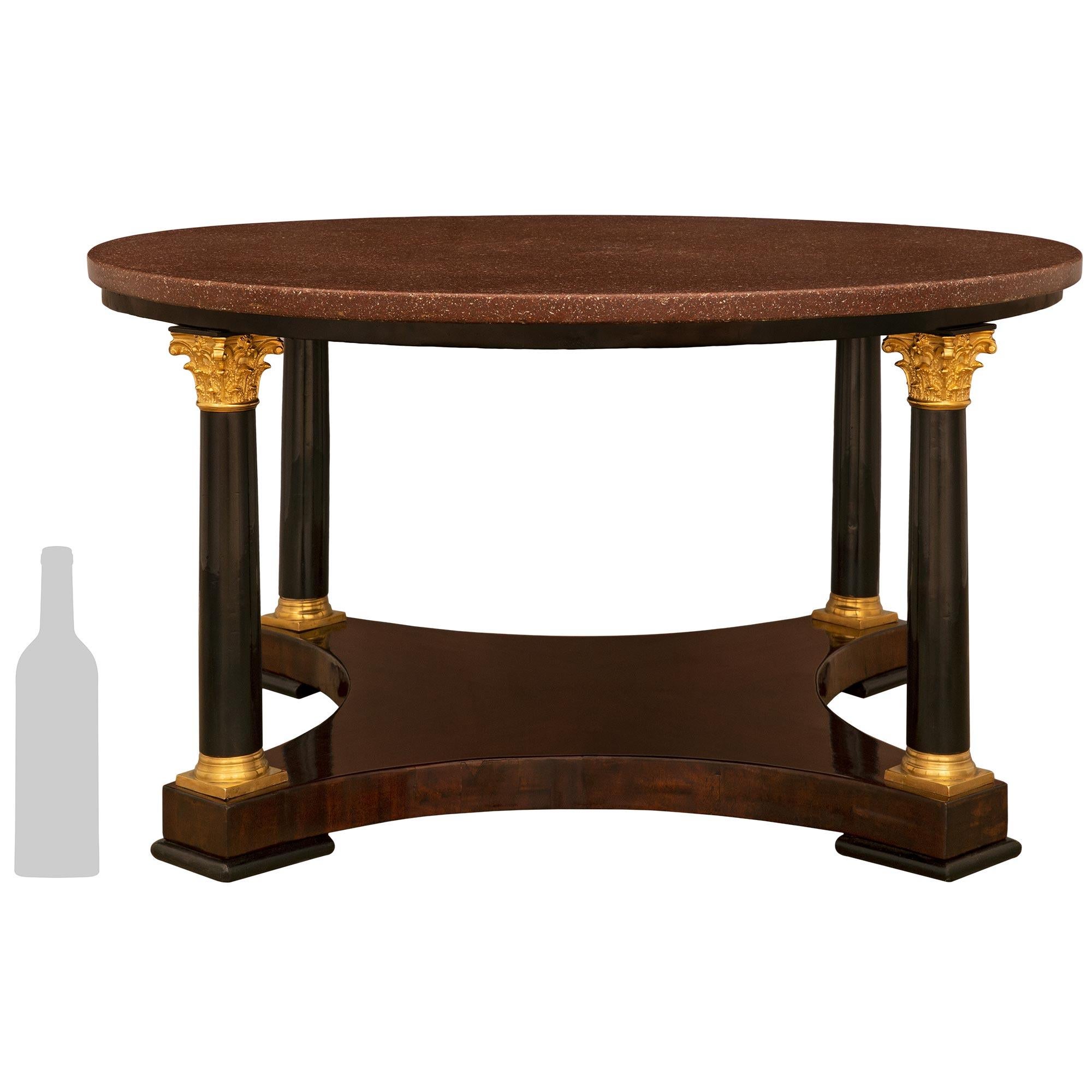 A handsome Continental 19th century neo-classical st. mahogany, ebonized fruitwood, ormolu and porphyry coffee table. The table is raised on four square feet below a mahogany bottom tier with concave sides and four ebonized fruitwood columns with