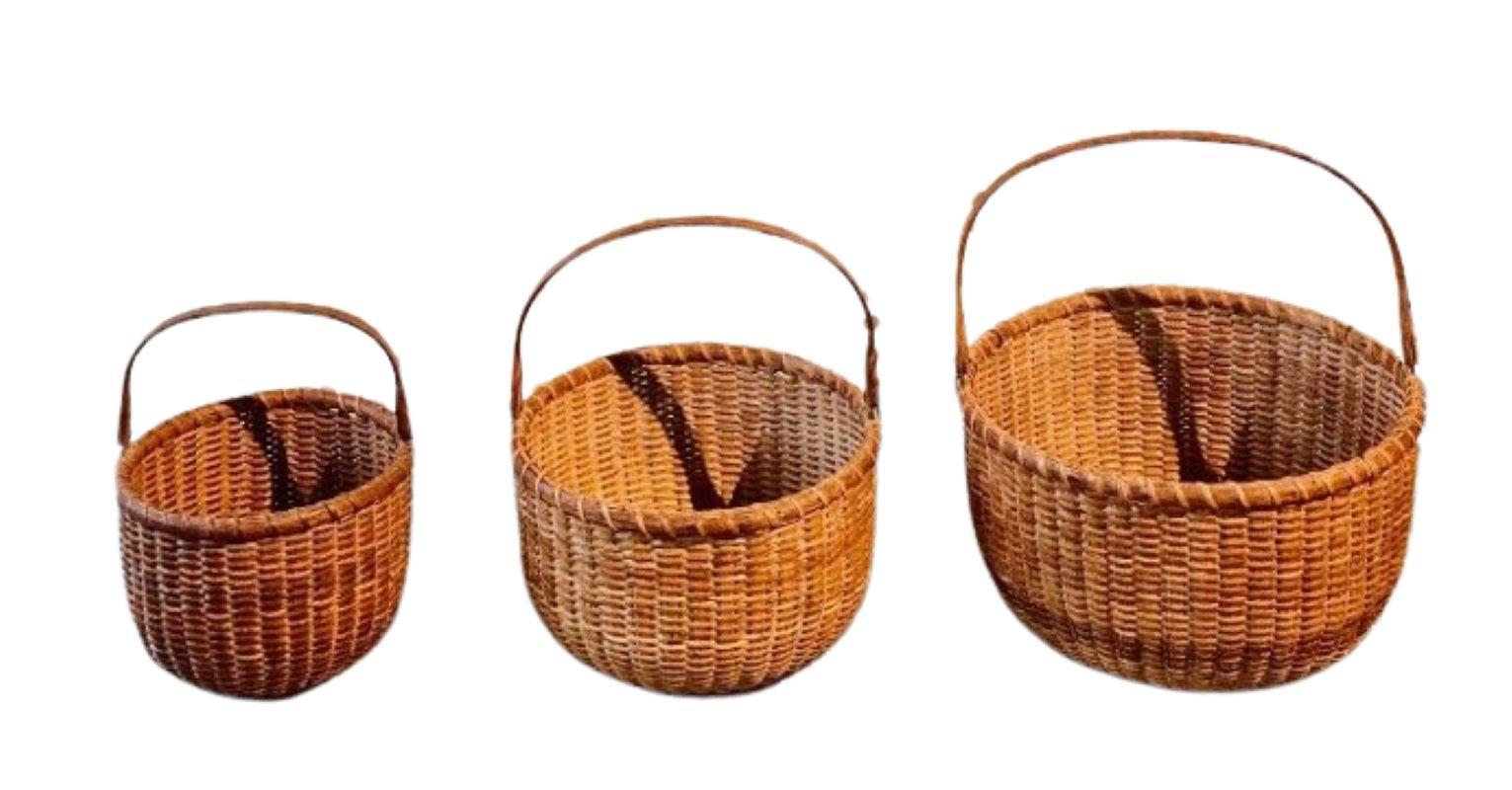 19th Century Nest of Three Nantucket Lightship Baskets, circa 1880, a graduated set of three round, open baskets having cane weave on rattan staves, a carved swing handle with an elongated ovoid lozenge end connected to tin ears that extend down