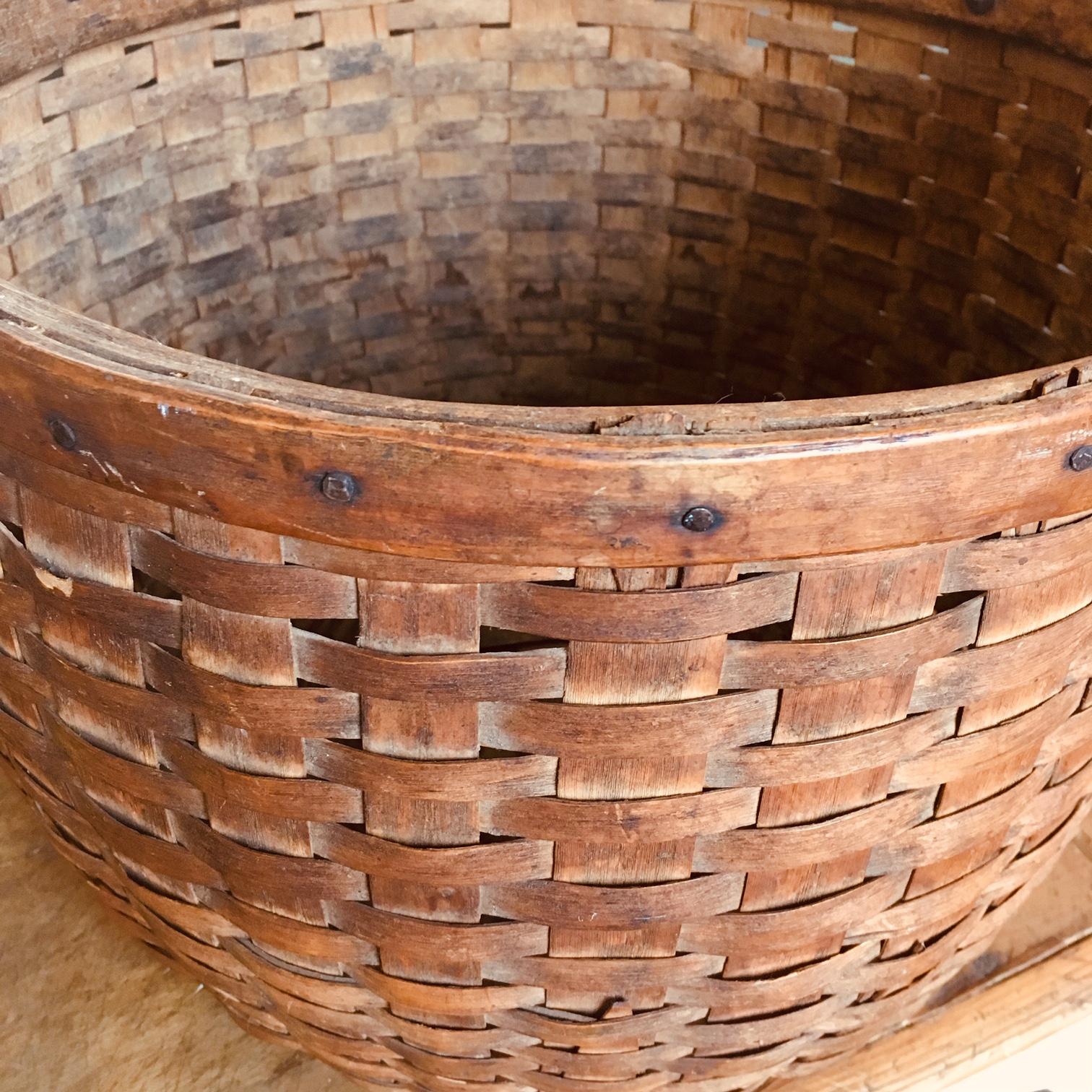 19th century New England woven splint bushel basket, circa 1880, having wide splint staves held between the split oak rim by square cut nails, and carved into a double arrow shape to cross each other on the bottom; the splint weave ends with an