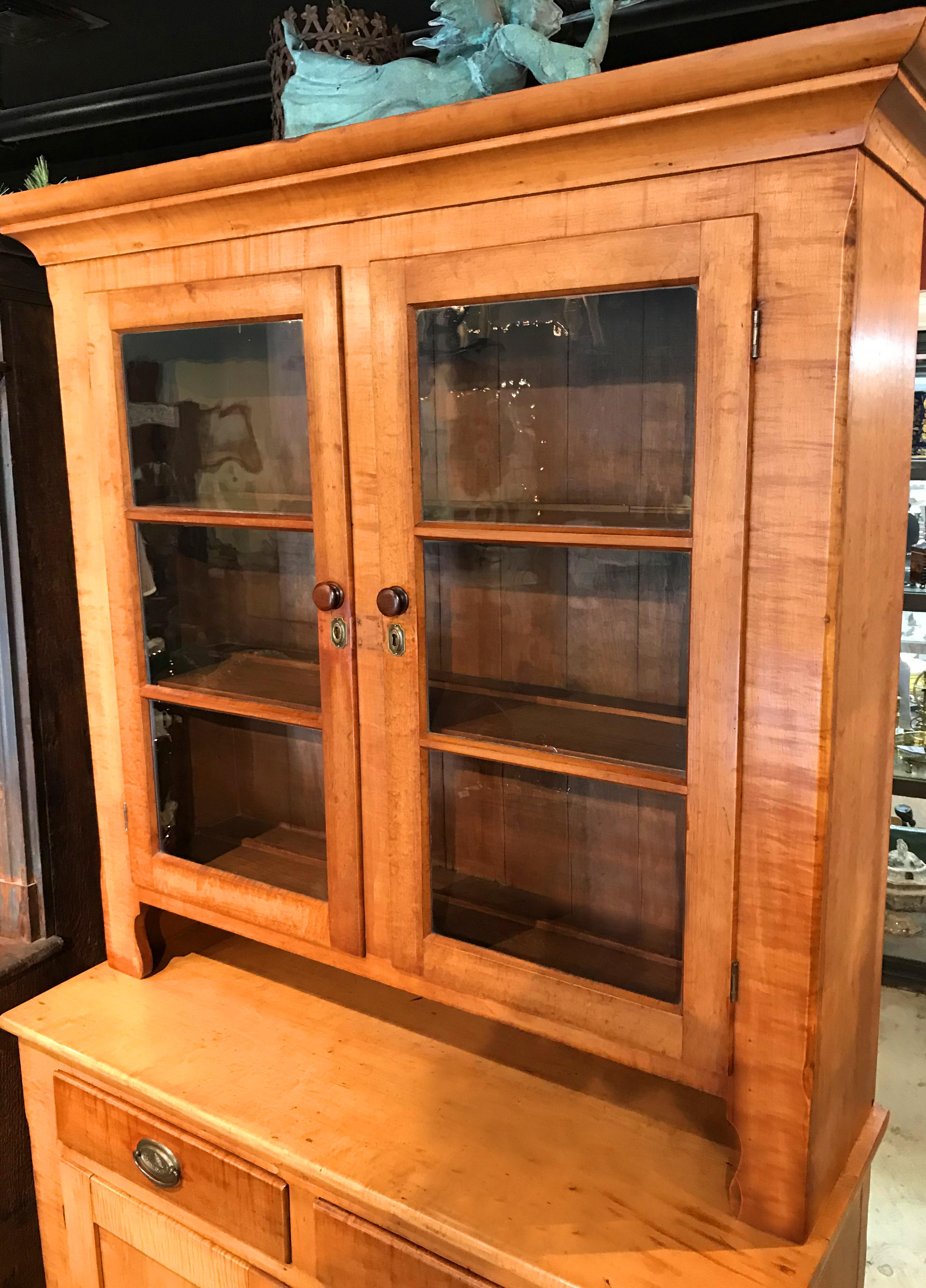A fine two-part tiger maple cupboard or hutch with molded cornice surmounting an upper case with two three-pane doors, which open to a three shelf interior with plate rails, over a lower case with two fitted drawers with decorative beehive brass