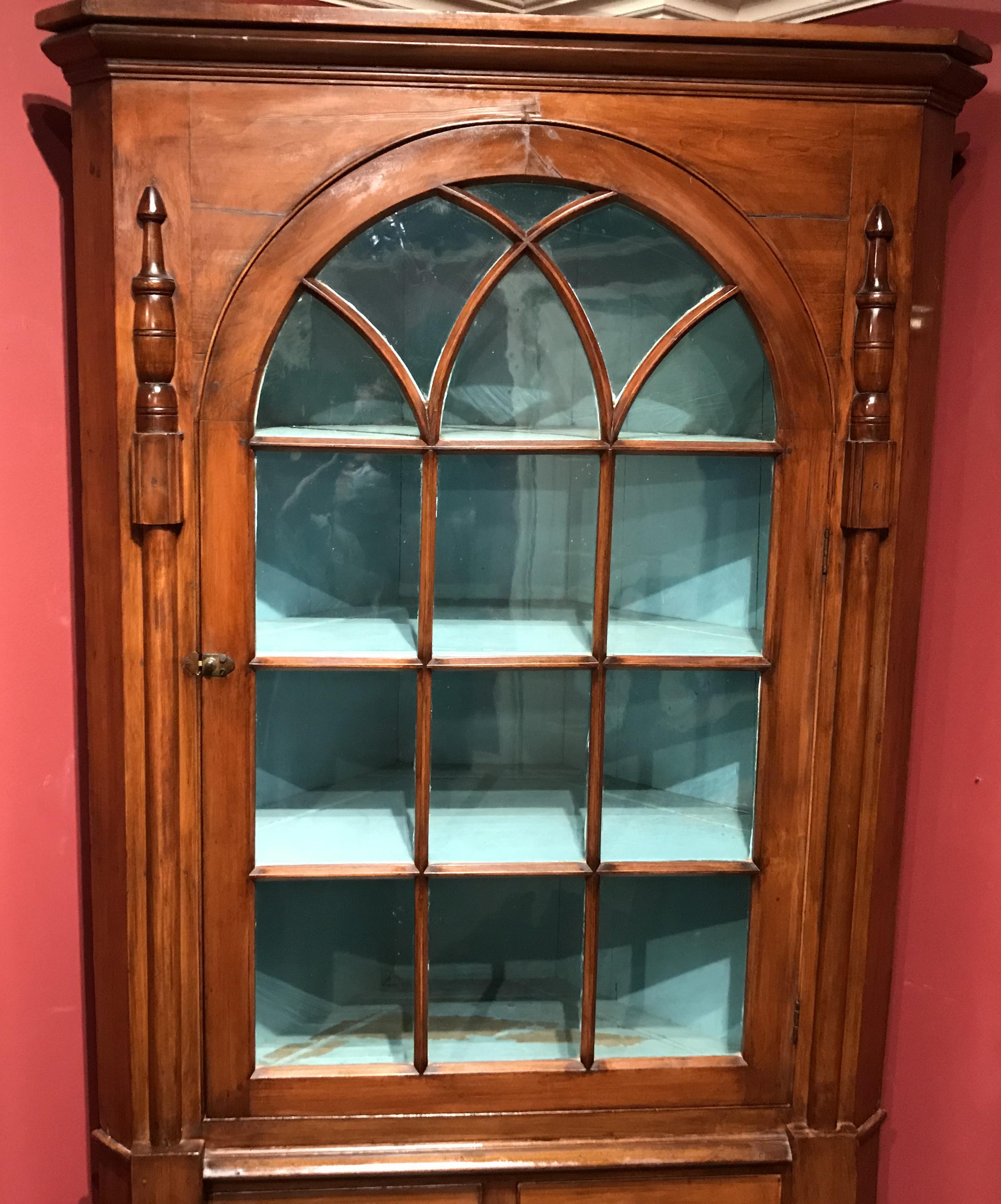 A fine two part cherry corner cupboard, the upper case with a molded cornice surmounting an arched glazed door, opening to a light blue painted three shelf interior, flanked by half rounded pilasters, over a lower case with two fitted drawers over