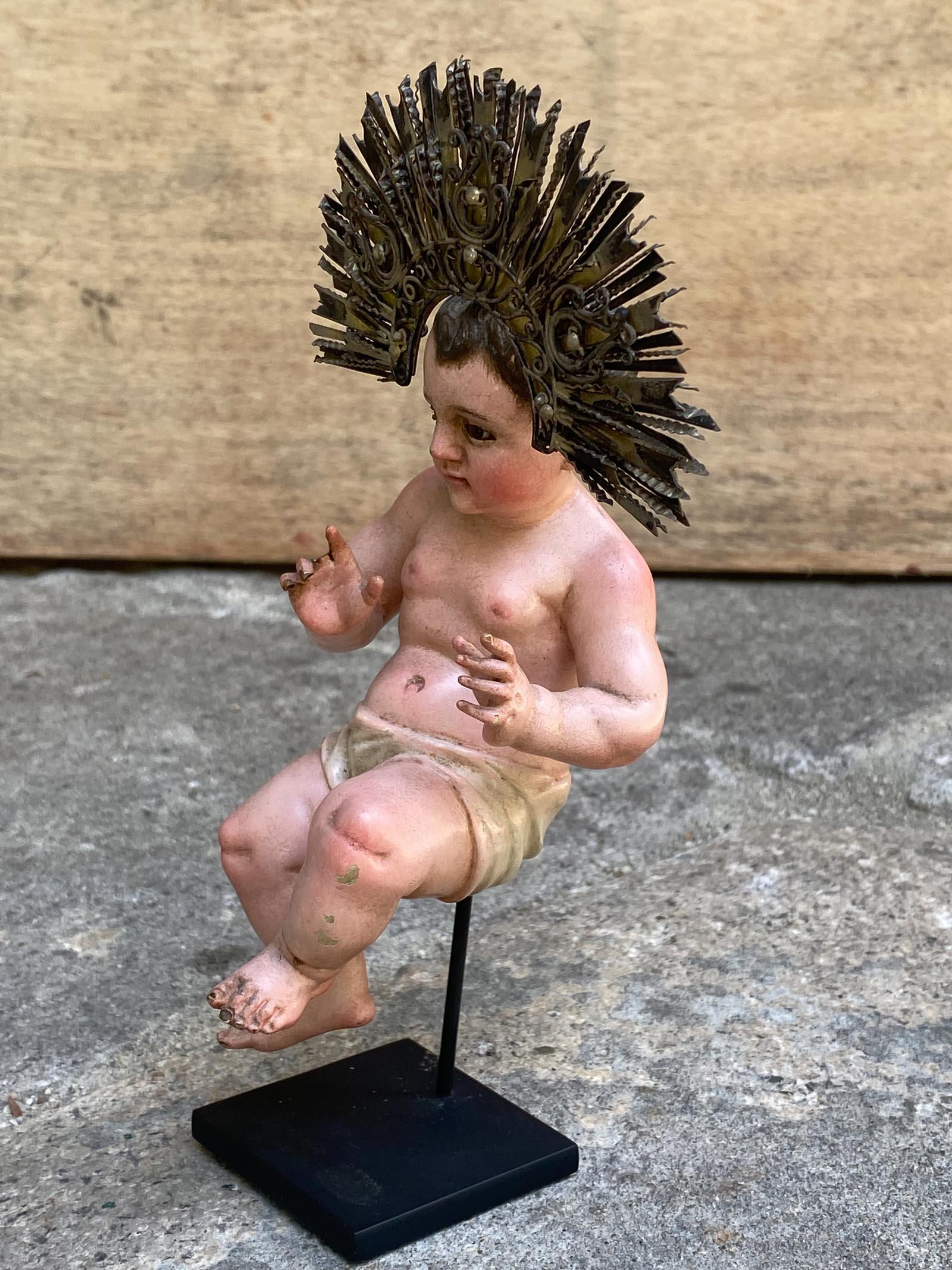 Una figura di Niño Jesús (Bambino Gesù) espressiva e finemente lavorata, proveniente dal Guatemala del XIX secolo, scolpita in legno con decorazioni policrome e occhi in vetro incastonati. La scultura raffigura il Bambino Gesù con le guance paffute,