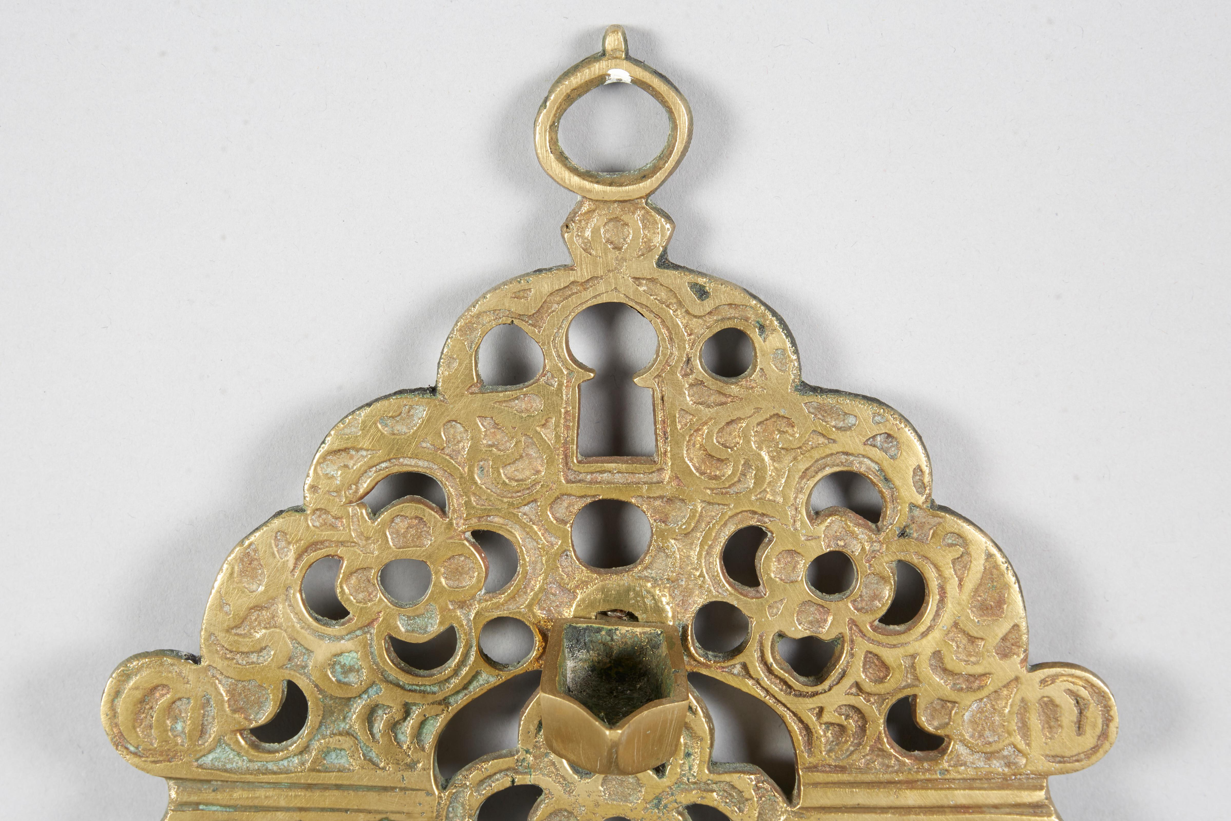 Cast brass Hanukkah Lamp, Morocco (probably, Sefrou), 19th century. 
A large flower in the center of the back plate (topped by the Shamash), surrounded by four smaller flowers. At the base of the back plate are five arched gates and at the top -