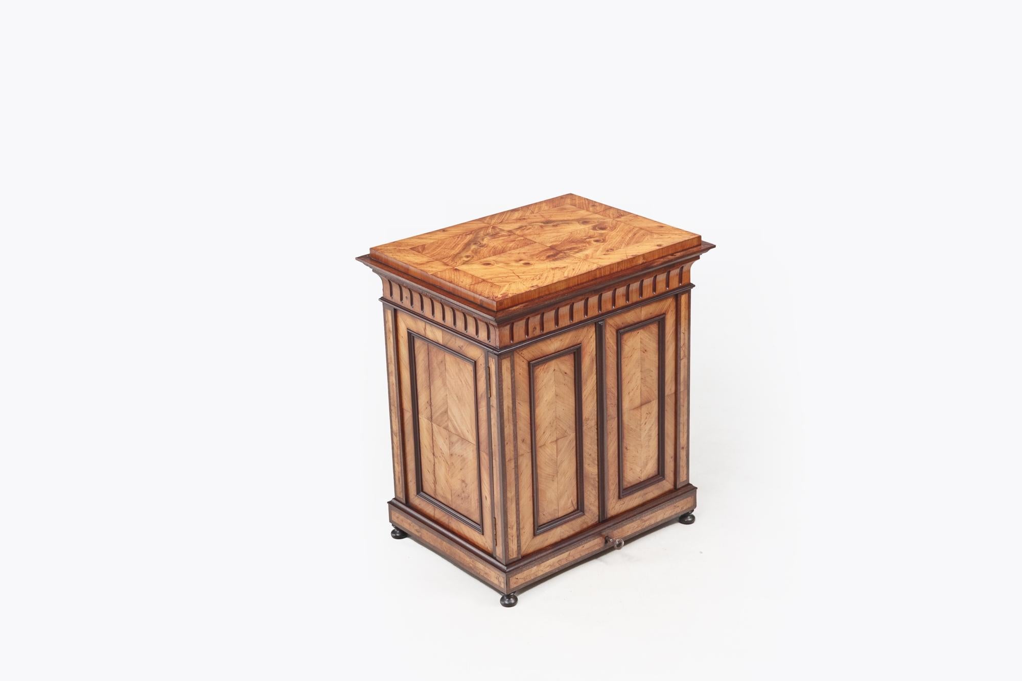 Armadio per esemplari in legno di noce e di frutta del XIX secolo con dettagli ebanizzati, cassetto sul fregio con motivo a reticolo e ante incassate a pannello che rivelano cassetti espositivi estraibili con pomelli ebanizzati. Heldly poggia su