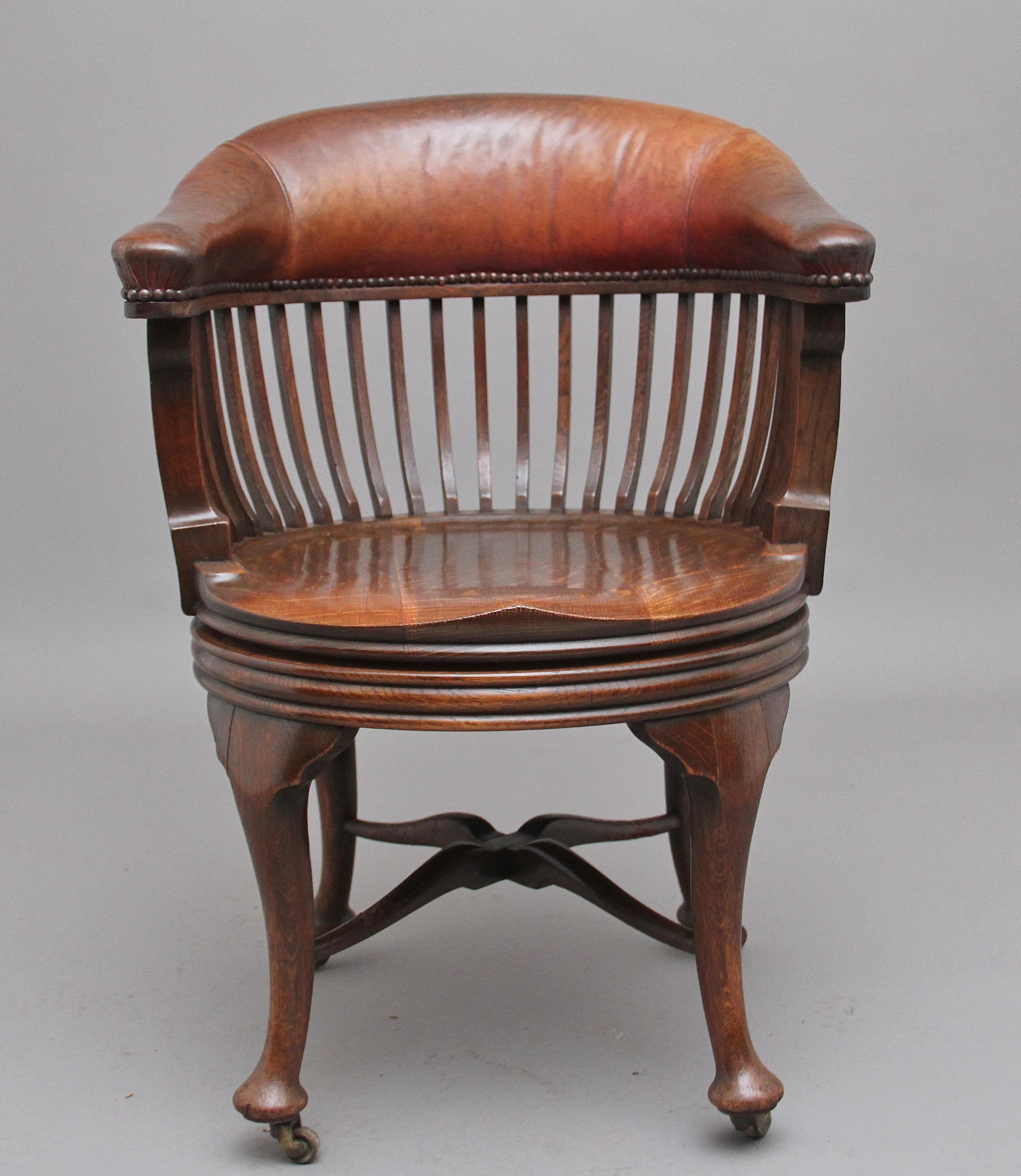 19th century oak and leather swivel desk chair, having a brown and red leather back support with brass stud decoration, finely shaped square upright supports, circular saddle seat with a reeded edge underneath, standing on shaped turned legs united