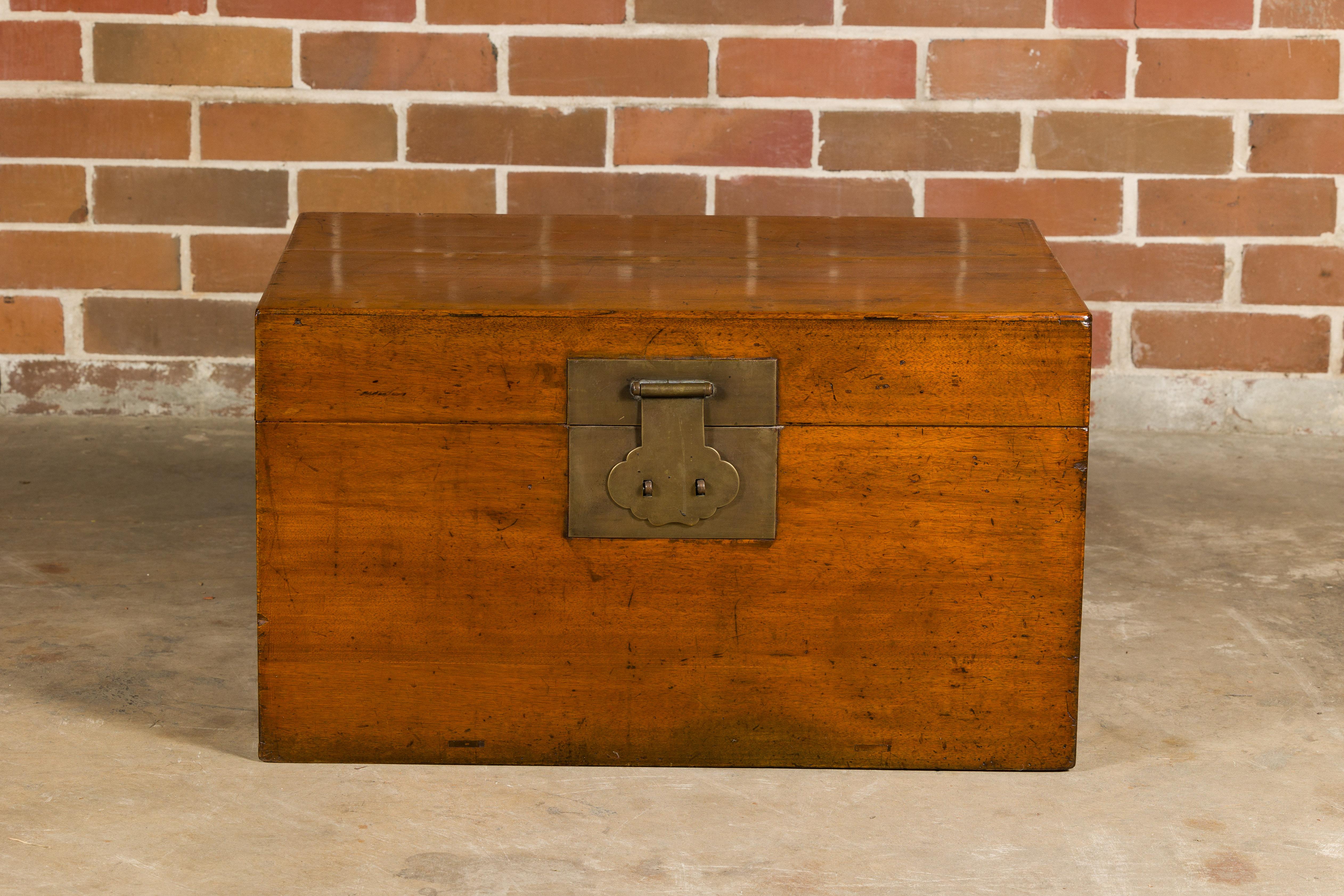 An oak or teak blanket chest from the 19th century with traditional brass lock, lateral handle and dovetail construction. Exuding an undeniable charm from the 19th century, this oak or teak blanket chest serves as a captivating blend of function and