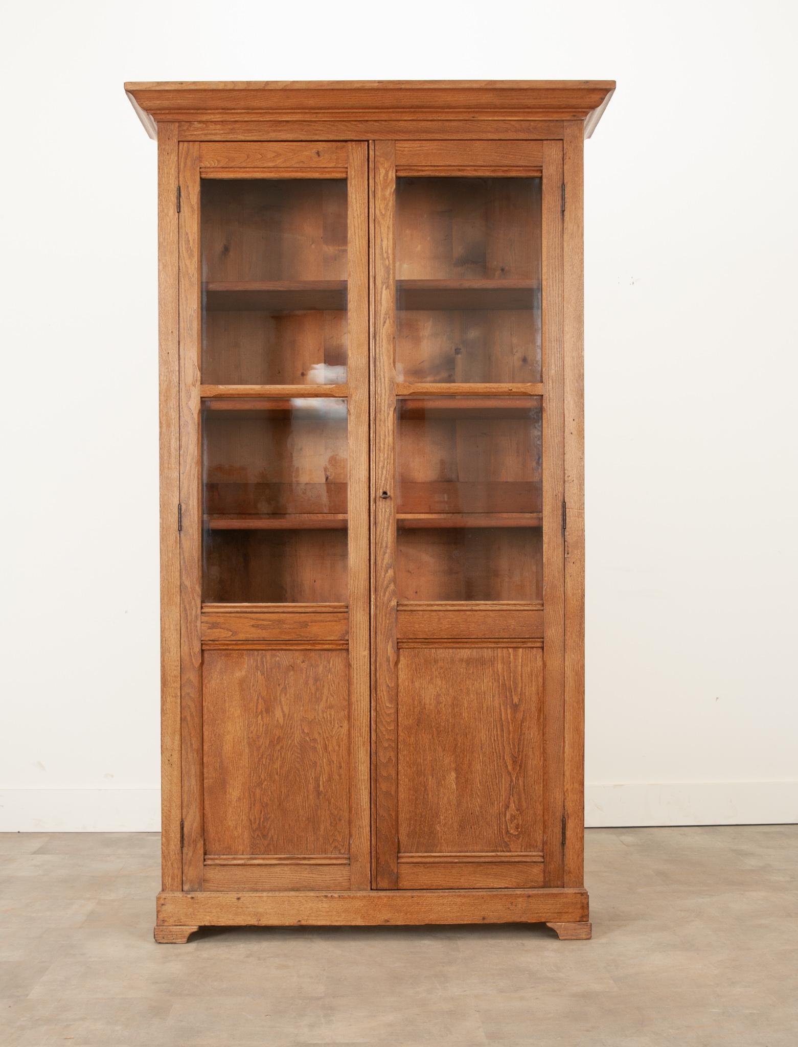 This solid oak bookcase pairs well with any style decor and has a raw oak finish. A sharp cornice tops the whole above a pair of glass front doors. The antique wavy glass provides a great view of the interior above simple paneling. Four adjustable
