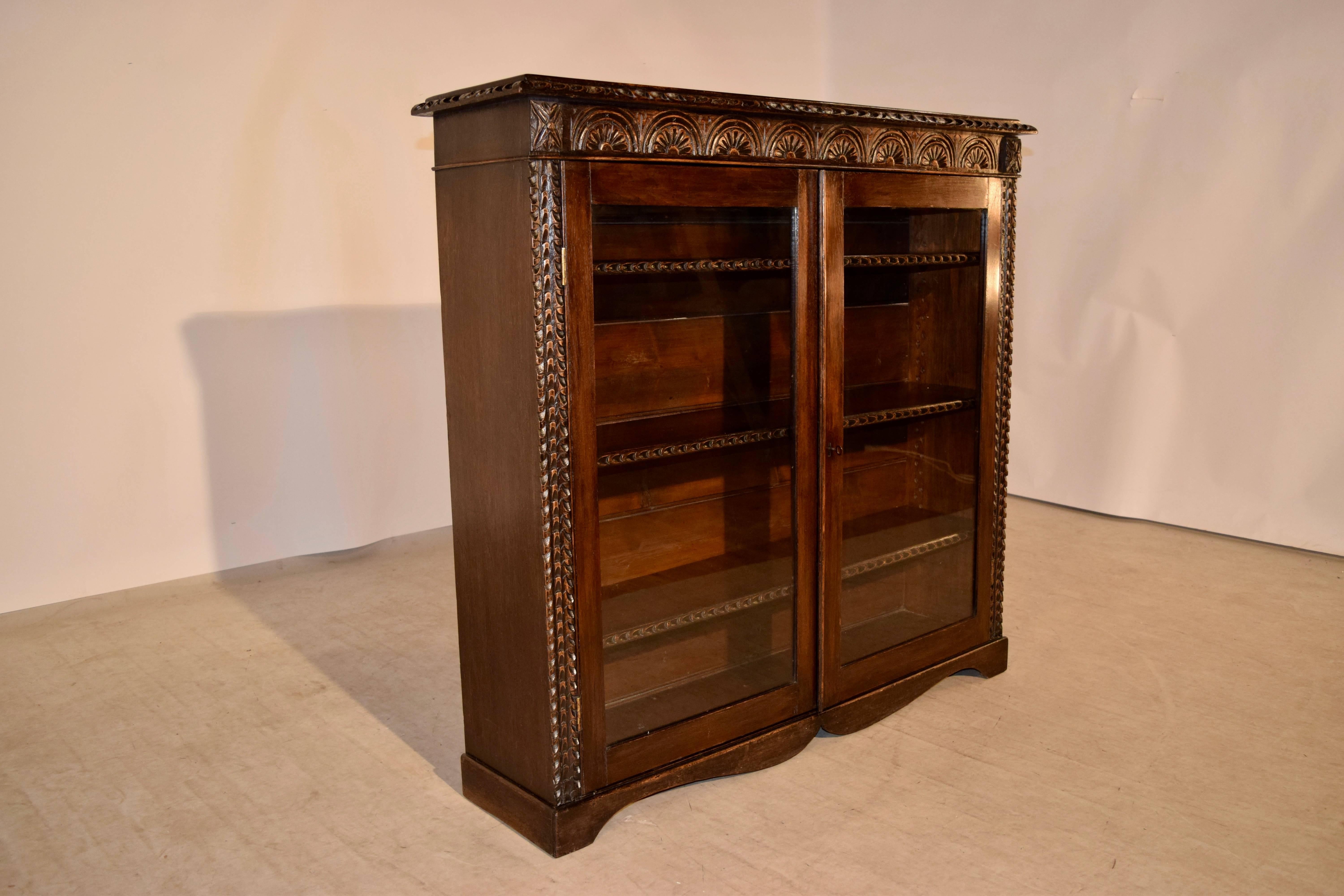 19th century English oak bookcase with glazed doors. The top is made from a single board and has a beveled and hand-carved decorated edge, which follows down to simple sides and a hand-carved apron in the front over two glazed doors, which are