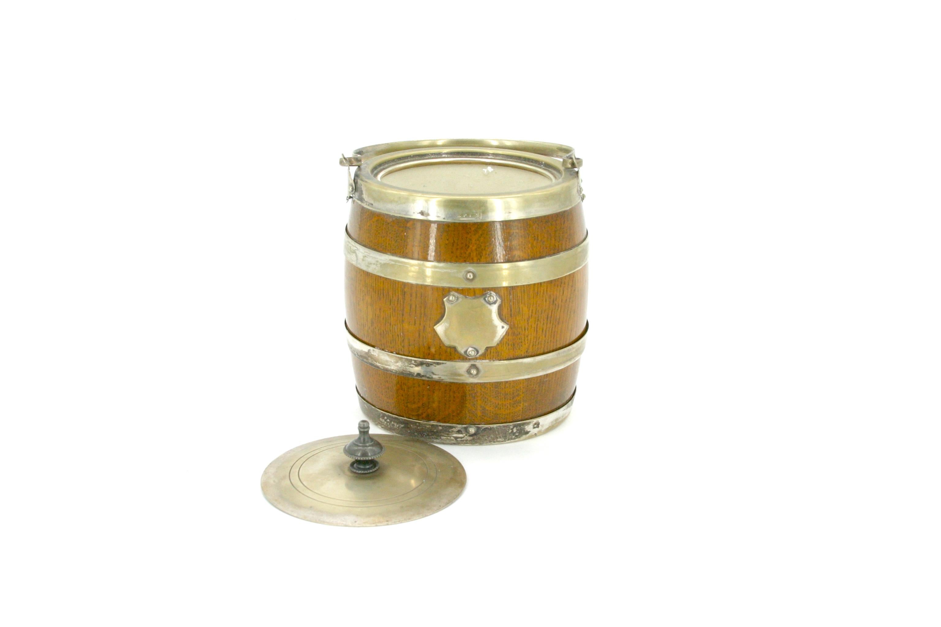 English oak with silver plated frame ice bucket / biscuit barrel with white interior ceramic liner. The biscuit box / ice bucket features a removable silver plate cover and holding top handle. It's in good antique condition with wear appropriate
