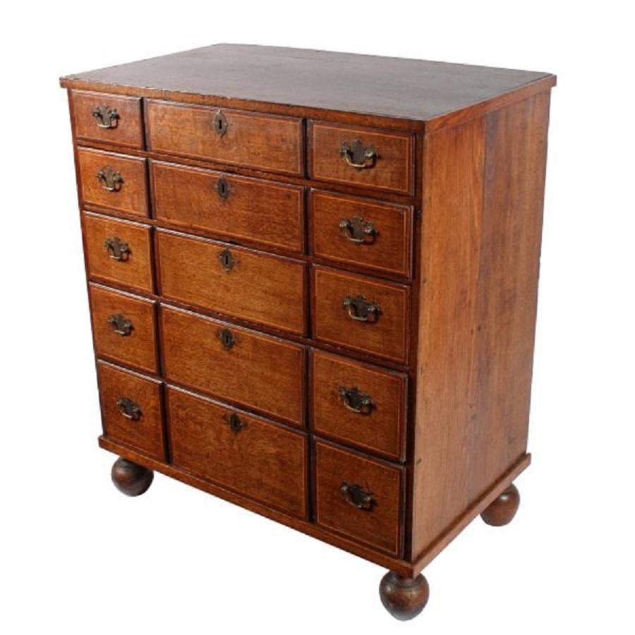 An early 19th century oak chest of drawers.

The chest has five graduated oak lined drawers with brass handles.

The drawer fronts are each made to look like three separate drawers and are cross banded and box wood strung.

Visually the chest