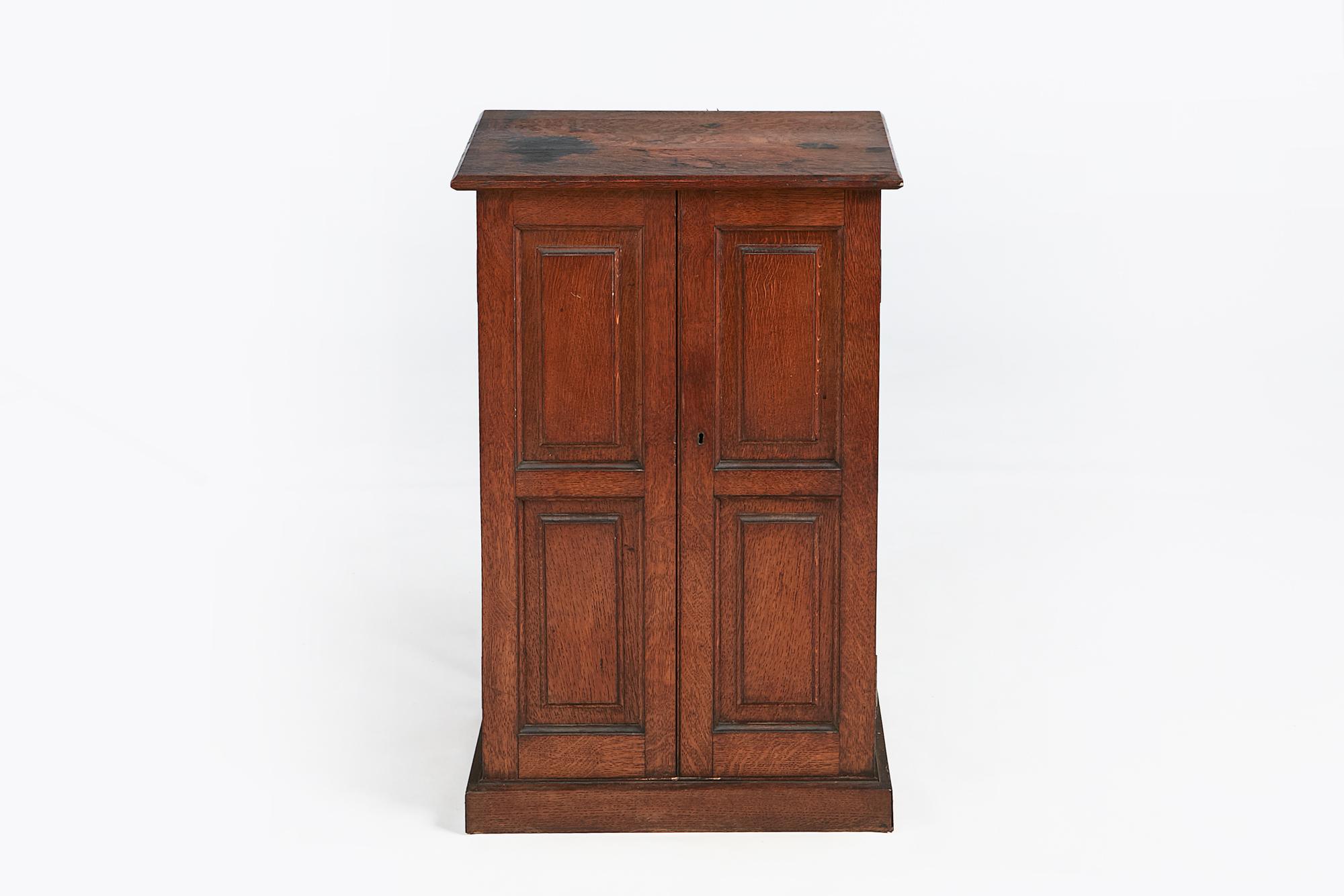 19th century oak coin cabinet, the moulded top above panelled body, the two front doors opening to reveal fitted interior of twenty two lined drawers terminating on platform base.