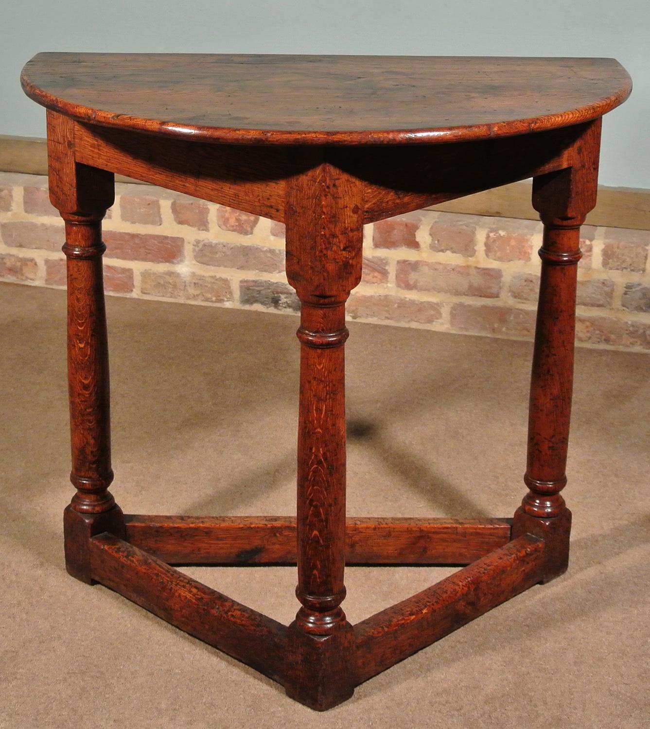 A most attractive 19th century oak credence style table of simple form on tapered gun barrel supports and co-joined stretchers. Some old worm tracks to surface (long dead), some very old bruises and dents. Peg jointed throughout with demilune top.